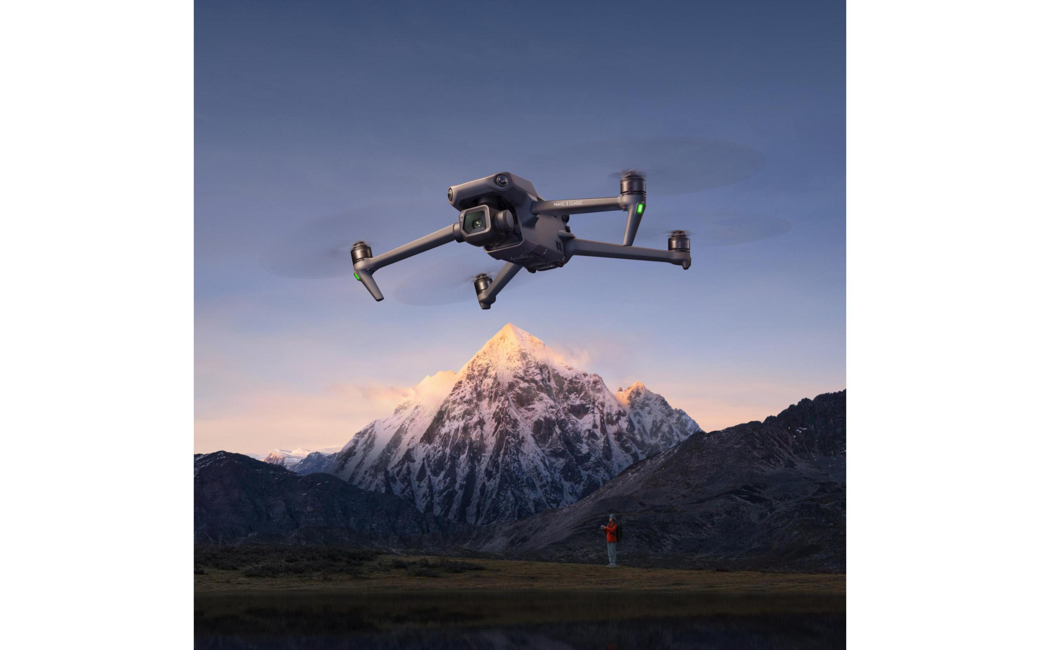 Dron volando sobre montañas. Una persona está en el suelo, con cámara. Cielo azul.