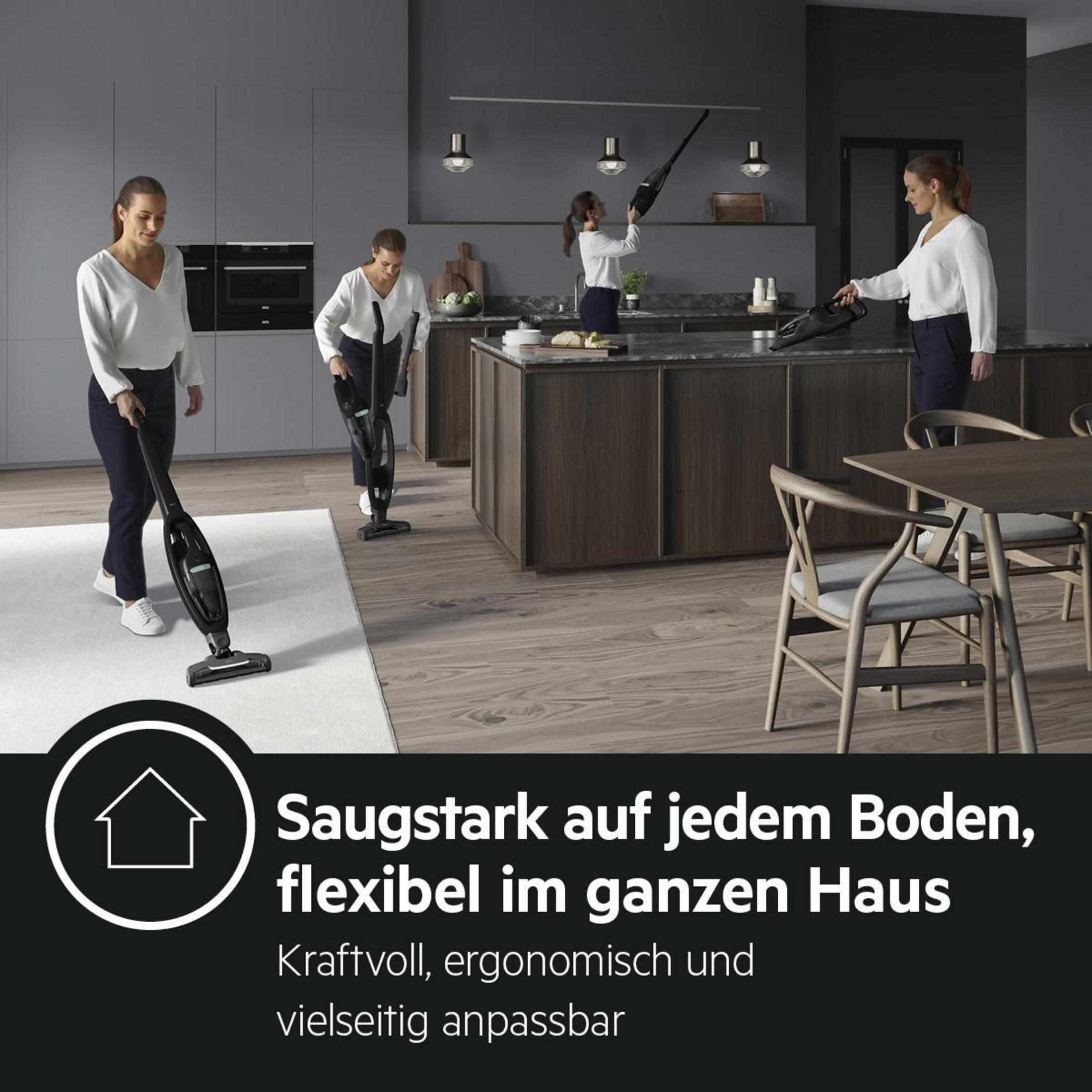 Vier Frauen benutzen schwarze, kabellose Staubsauger in einer modernen Küche mit grauen Schränken.
