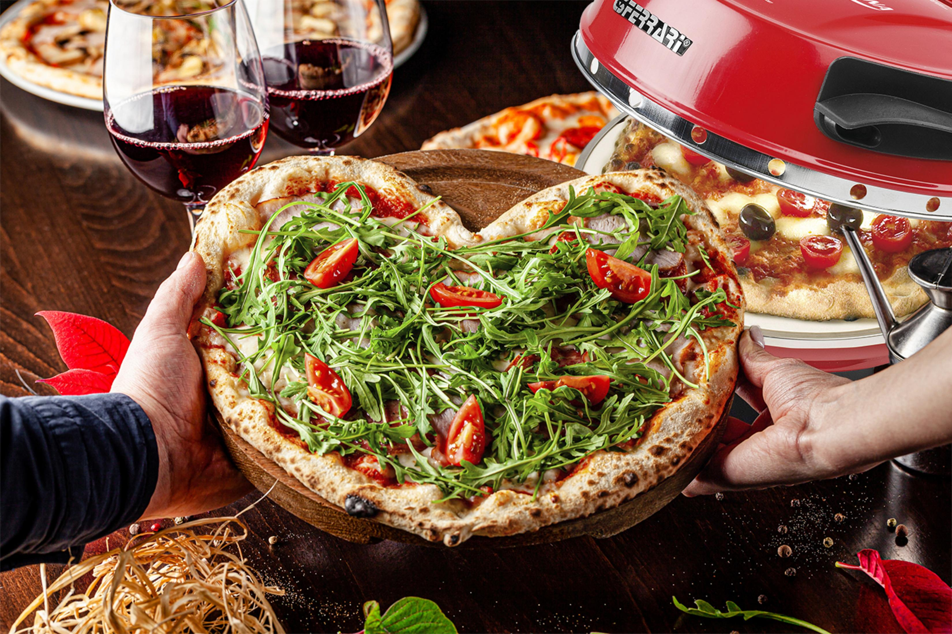 Una pizza en forma de corazón sostenida por dos manos. Pizza con rúcula y tomates, vino tinto y horno de pizza.