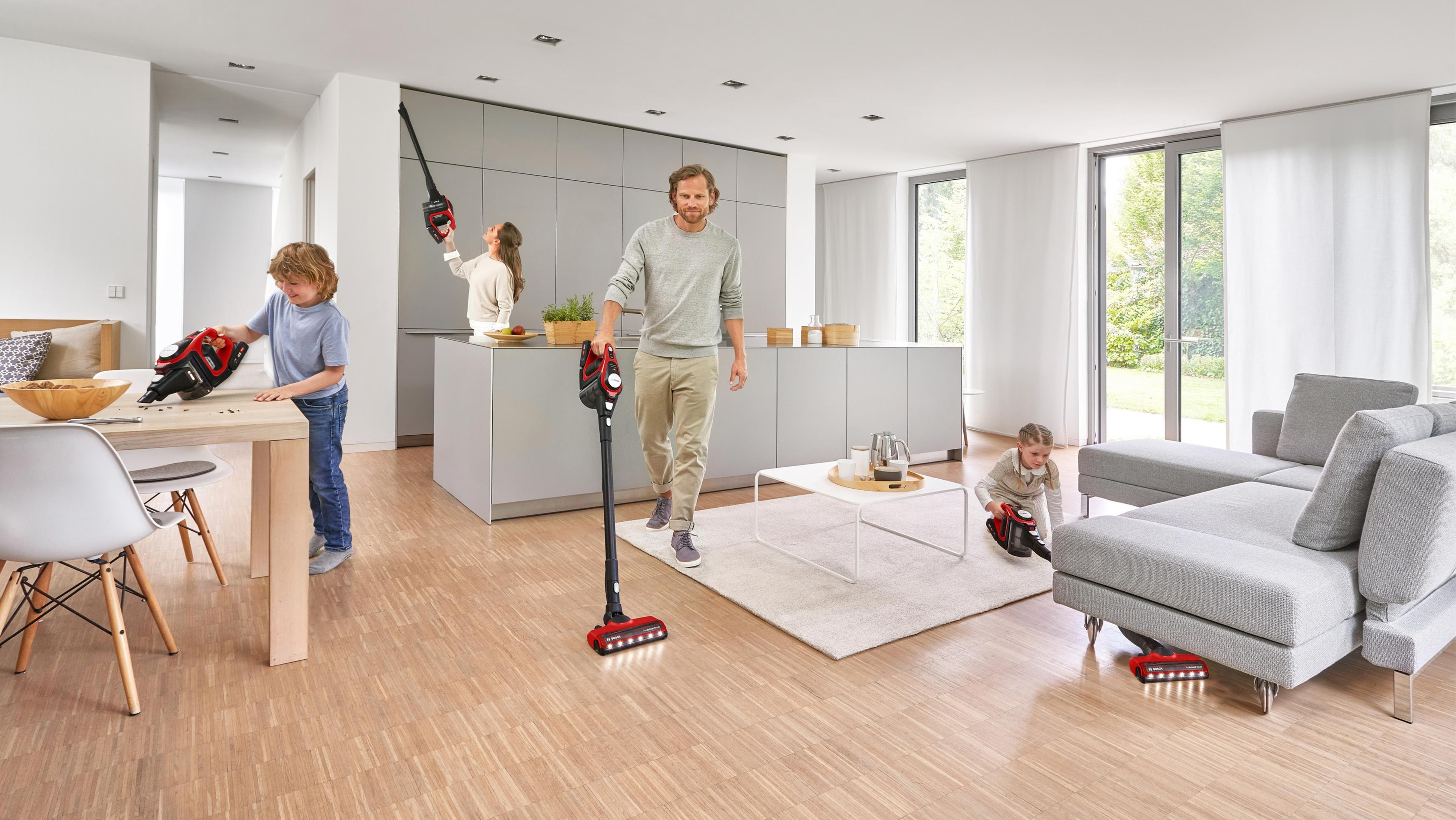 Eine Familie reinigt ein modernes Zuhause mit rot-schwarzen Akku-Staubsaugern.