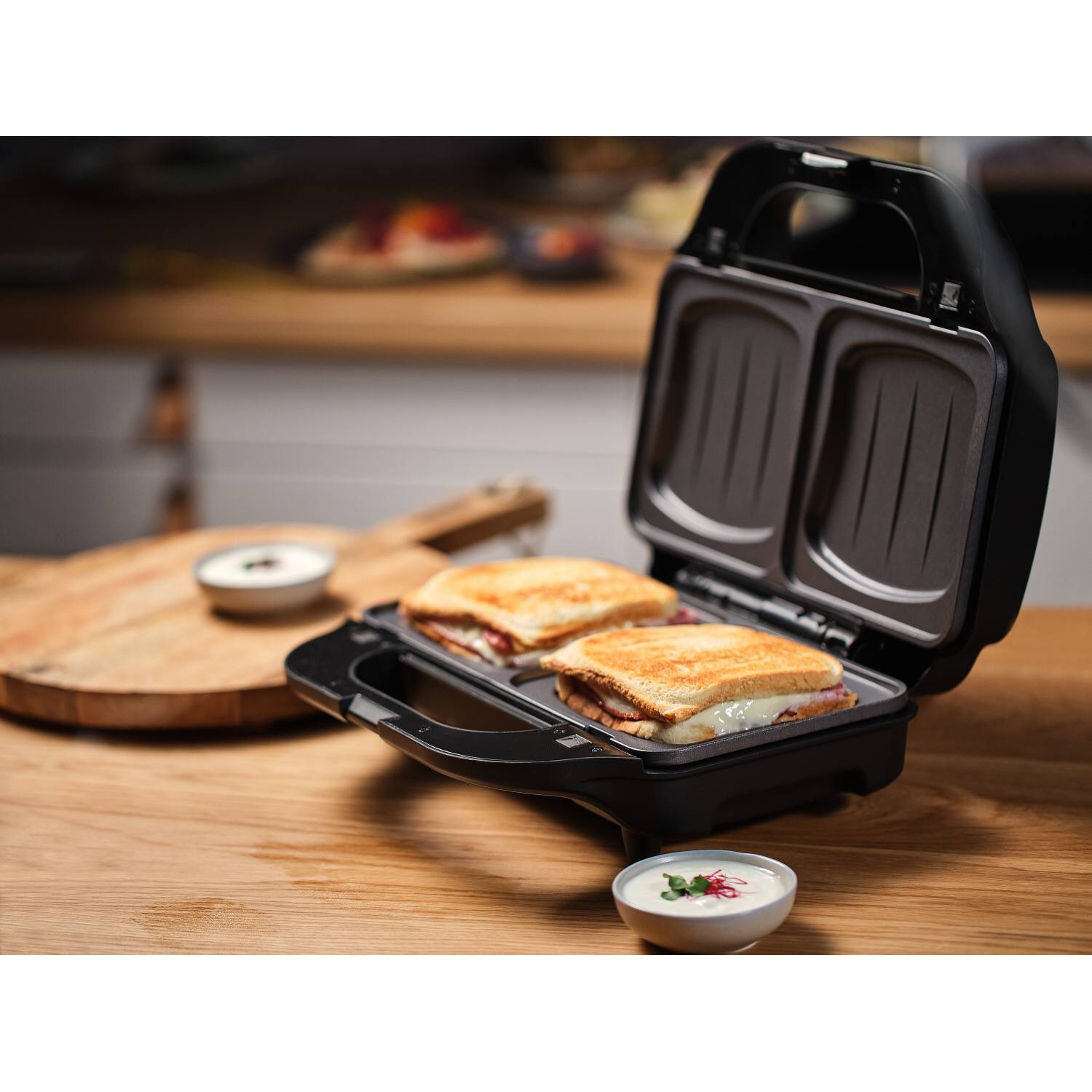 Sandwiches in einem schwarzen Sandwichmaker mit Soßen daneben.