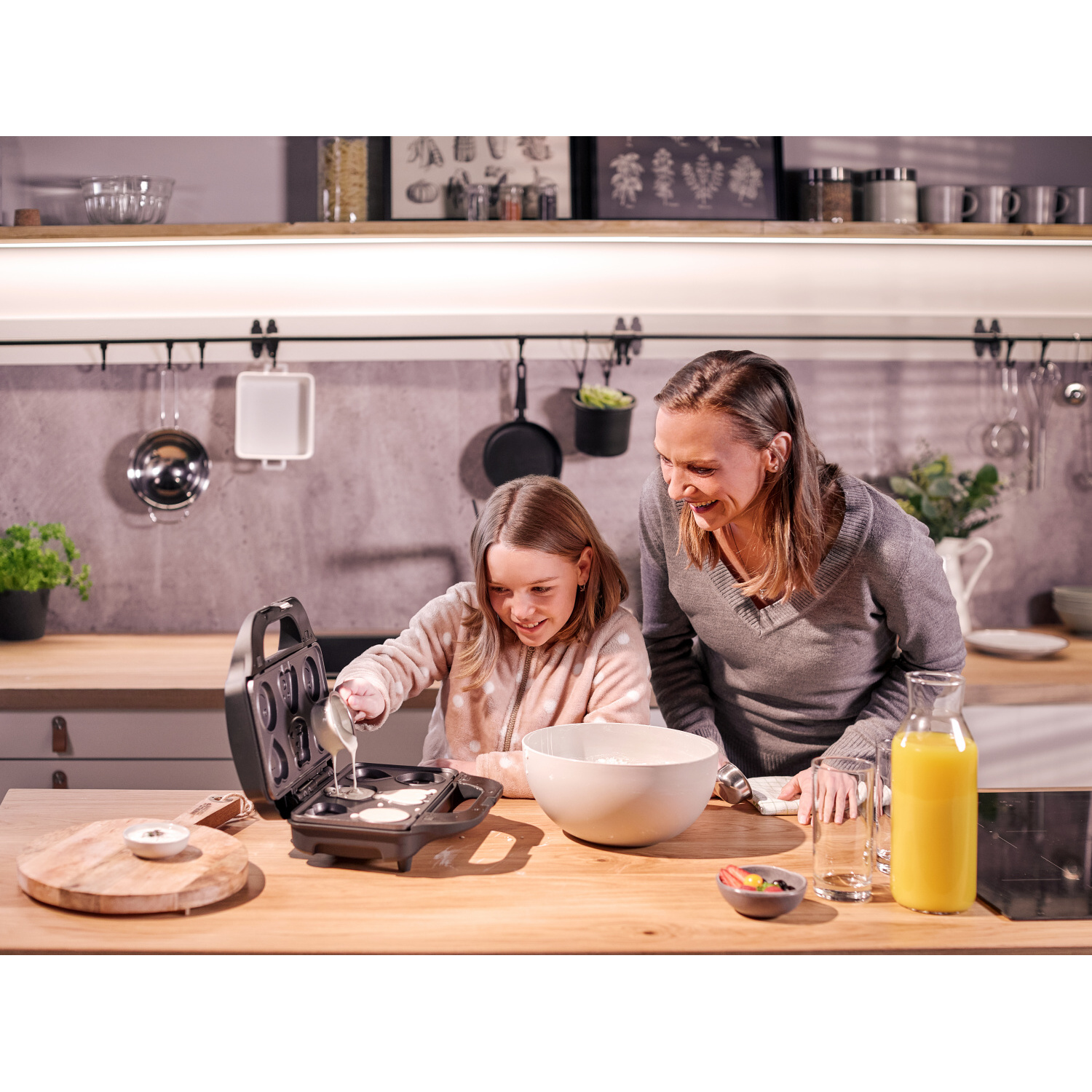 Frau und Mädchen machen Waffeln, gießen Teig ein. Küchenszene.