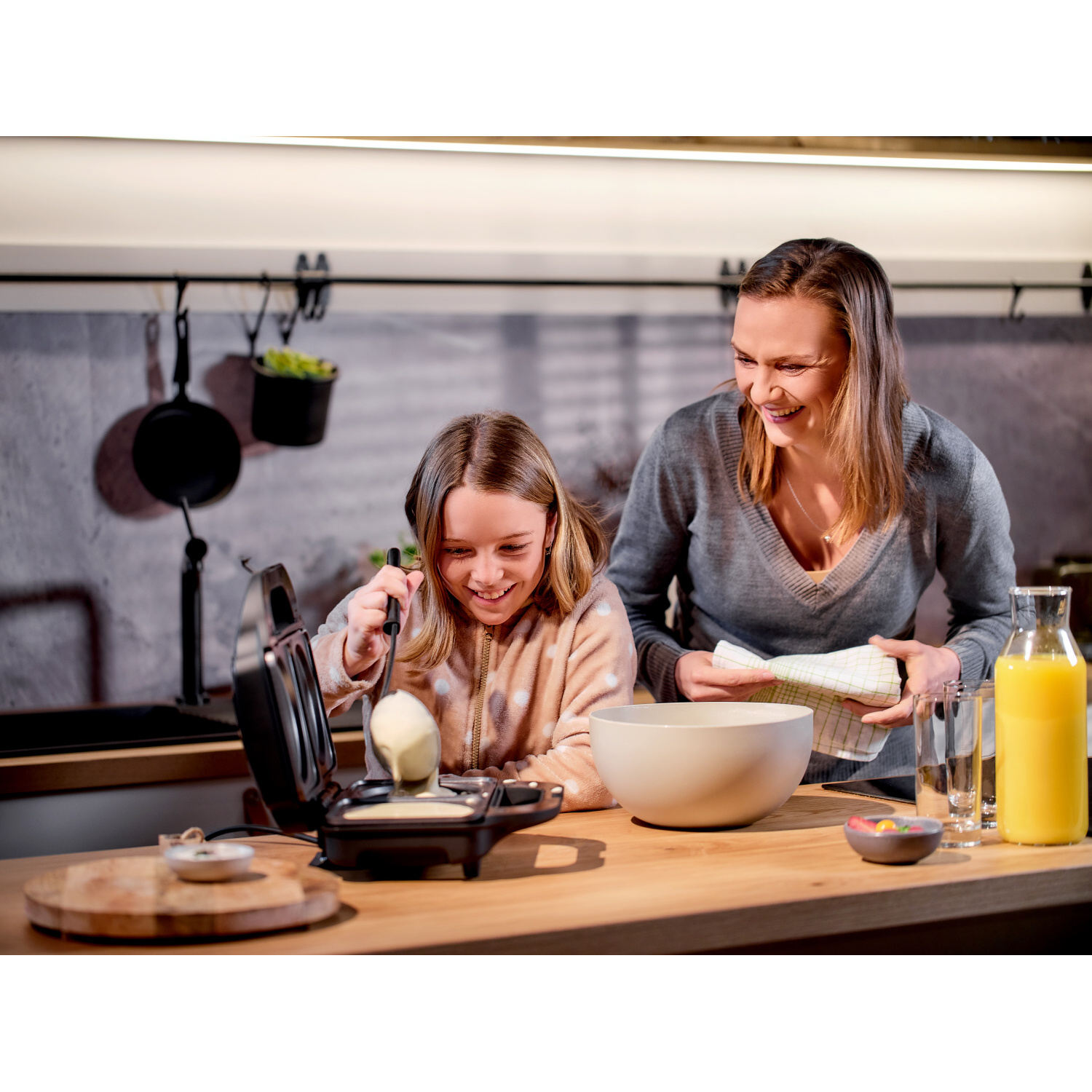 Mujer y niña haciendo gofres con una gofrera en un entorno de cocina.