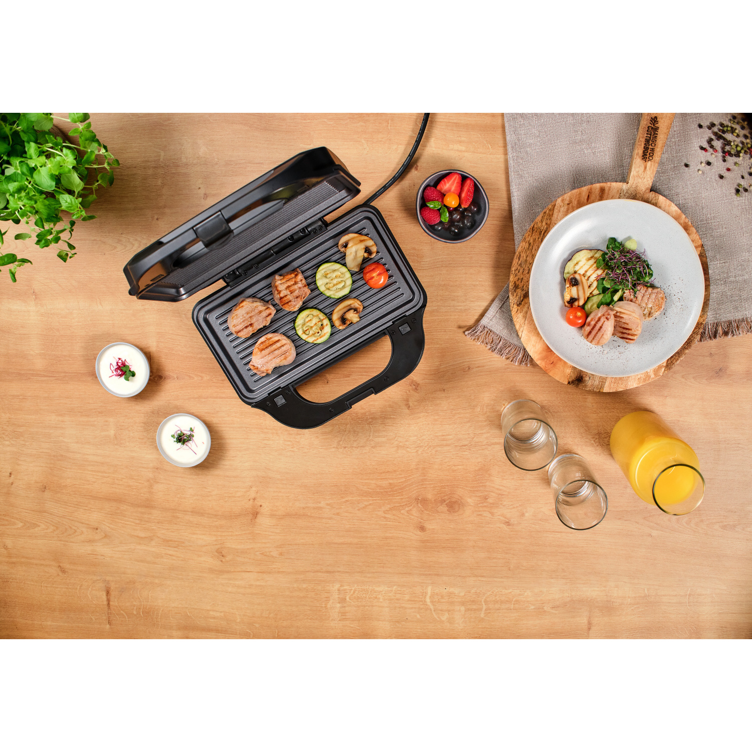 Una parrilla con comida cocinada, junto a platos de comida y cuencos en una mesa de madera.