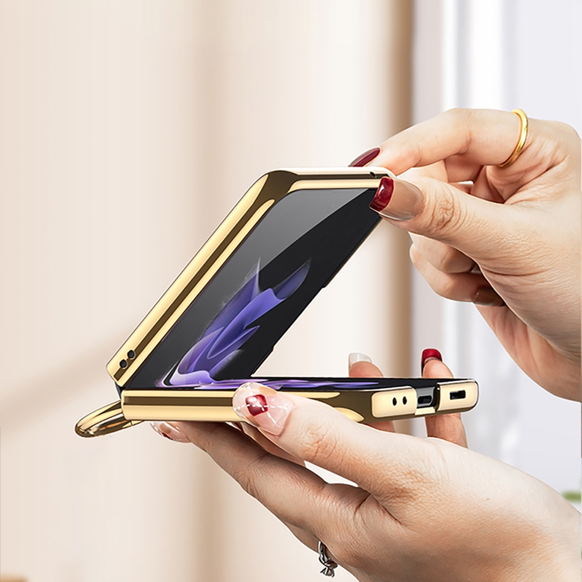 Hände halten ein goldenes Telefon und klappen es auf. Roter Nagellack ist sichtbar.