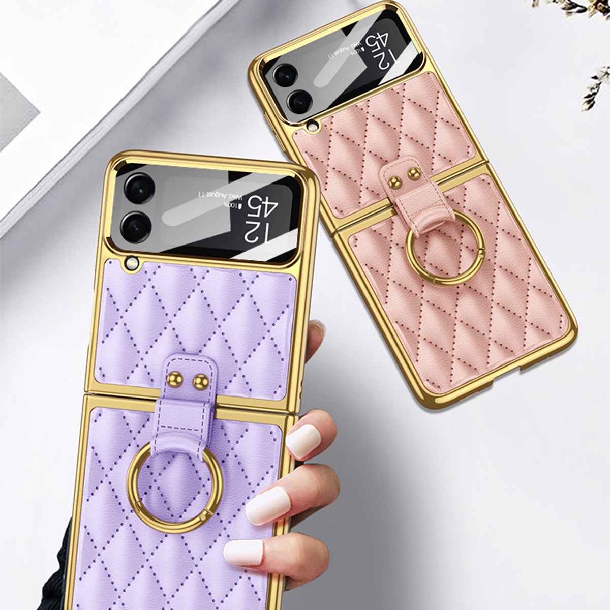 Zwei faltbare Handyhüllen, eine lila, eine rosa. Beide haben goldene Verzierungen und Ringhalter. Von Hand gehalten.