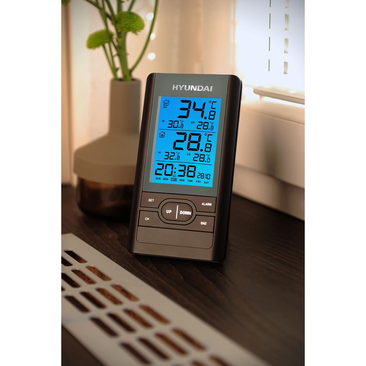 Digitalanzeige mit Temperatur und Uhrzeit, Tasten, Vase und Lüftung im Hintergrund.