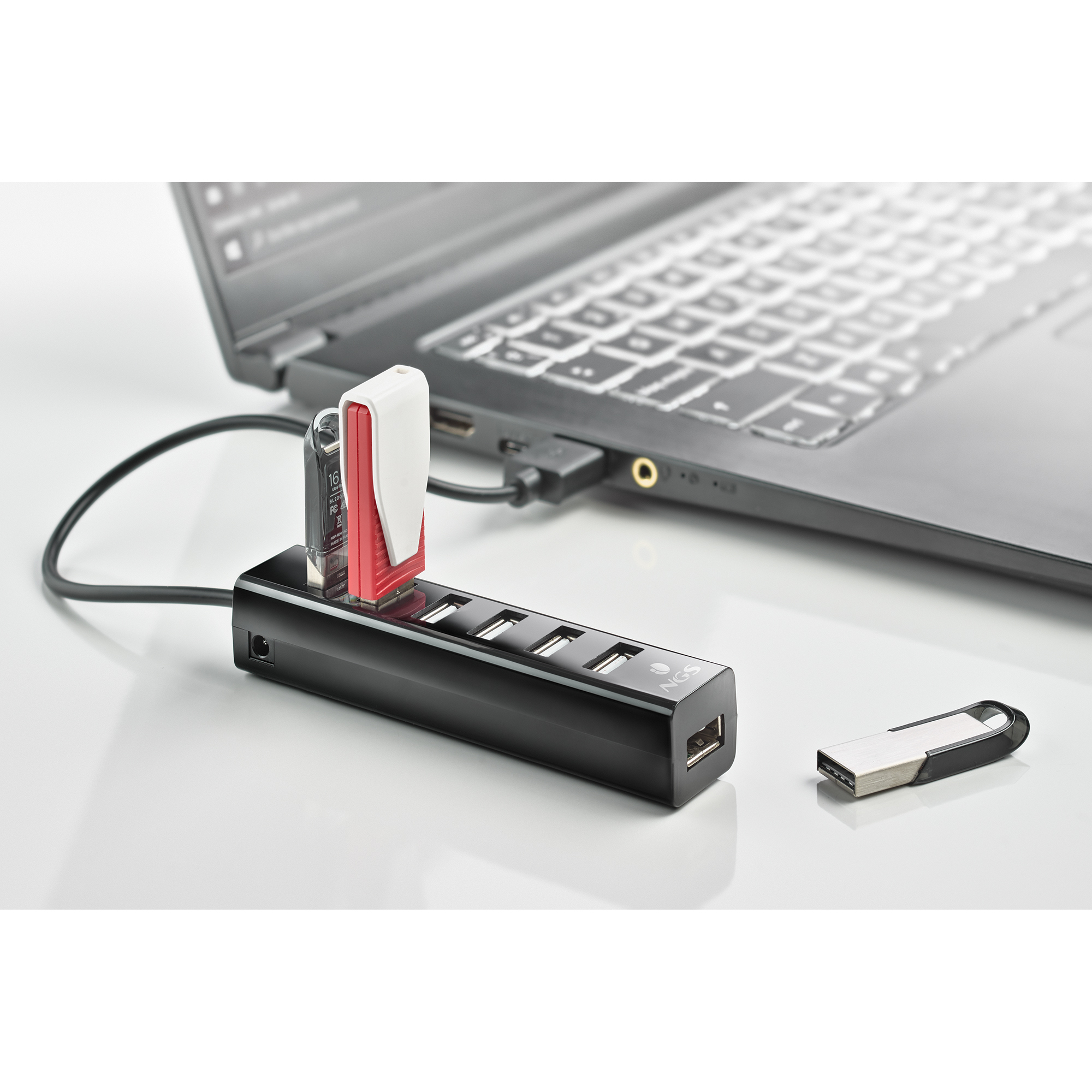 Ein schwarzer USB-Hub, der mit einem Laptop verbunden ist, mit zwei USB-Laufwerken, auf einer weißen Oberfläche.