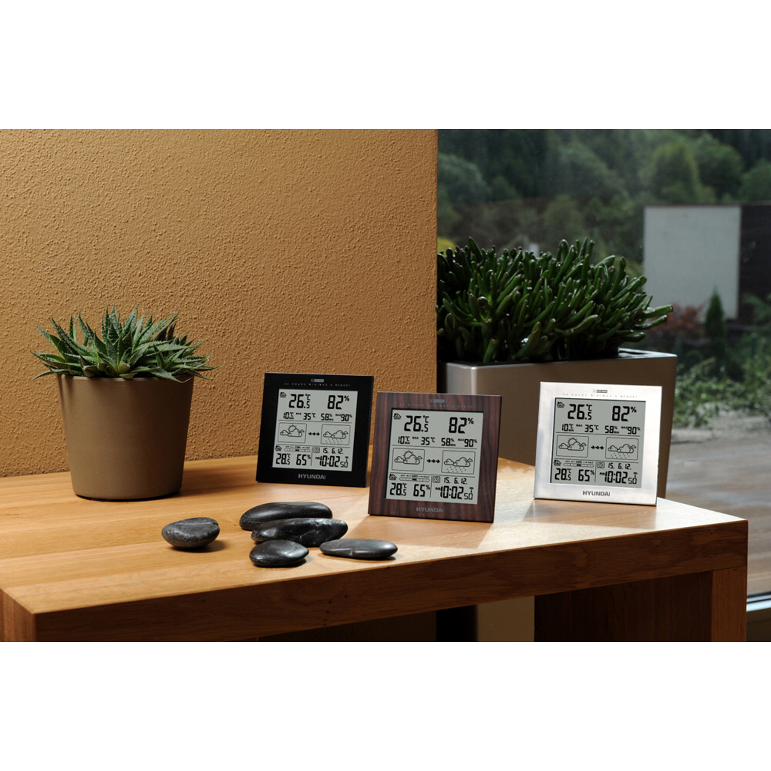 Drei digitale Wetterstationen auf einem Tisch mit Dekoration und Hintergrund.
