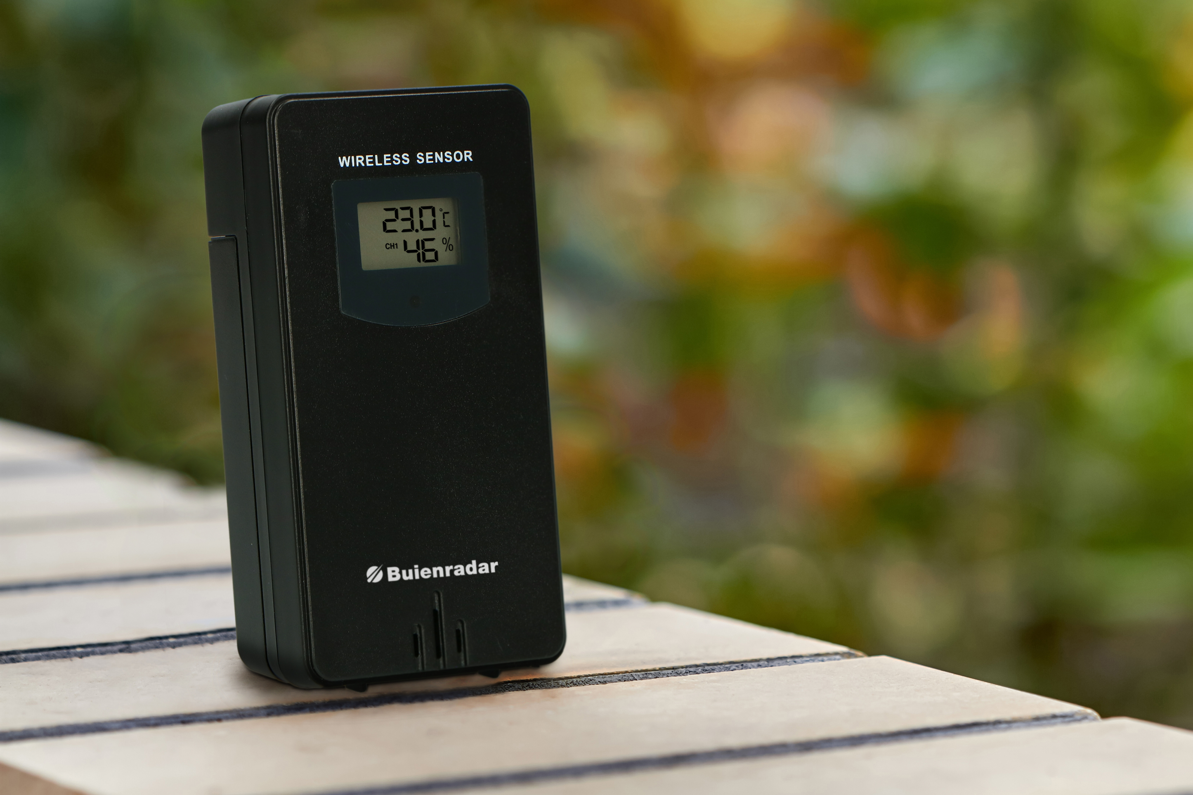 Schwarzer Wettersensor auf Holz, zeigt Temperatur und Luftfeuchtigkeit.