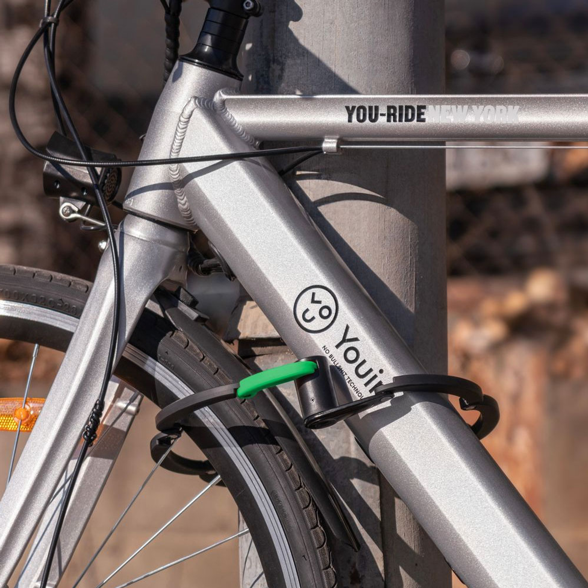 Bicicleta plateada asegurada a un poste; logotipo de You-ride New York visible.
