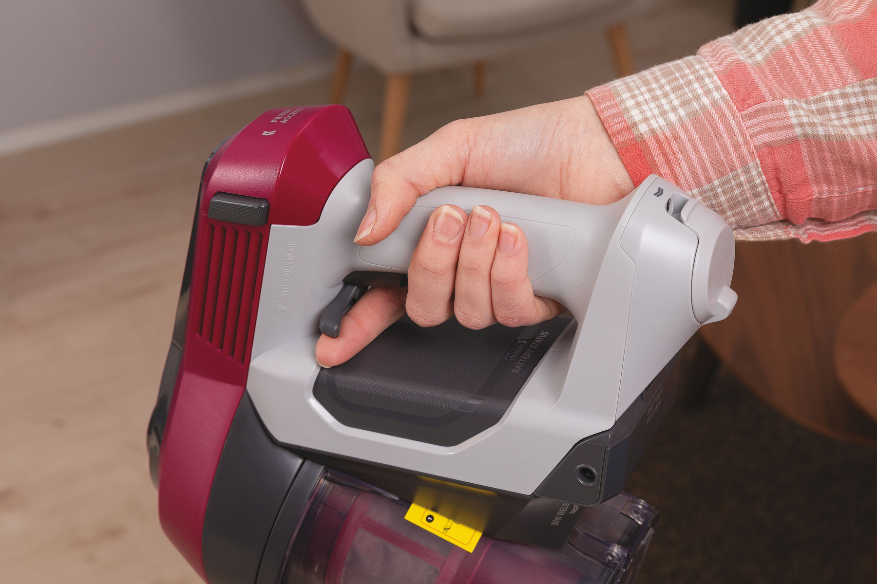 Die Hand einer Person, die einen rot-grauen kabellosen Staubsauger hält. Der Griff hat einen Auslöser.