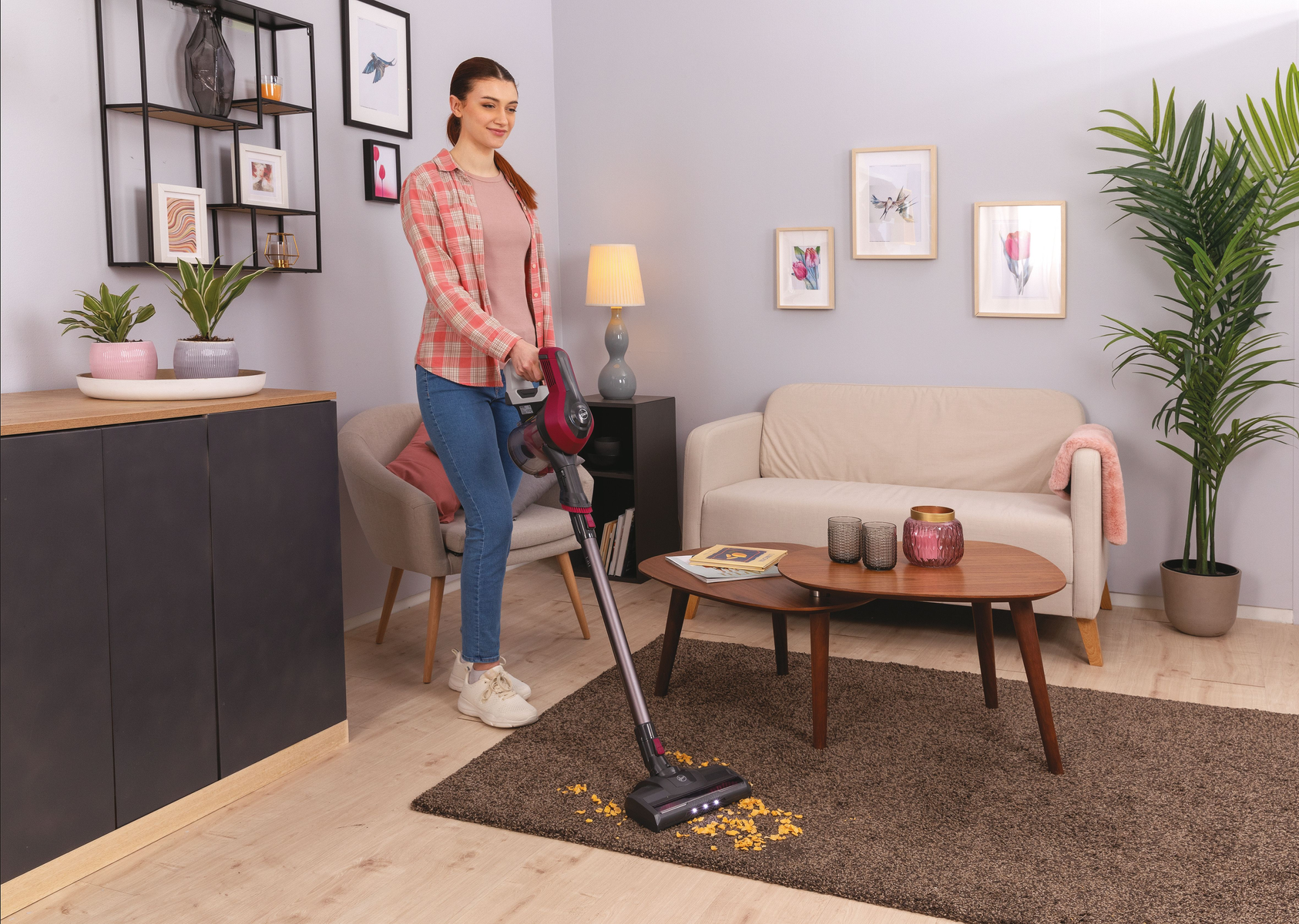 Eine Frau saugt in einem Wohnzimmer mit einem modernen Staubsauger einen Teppich.