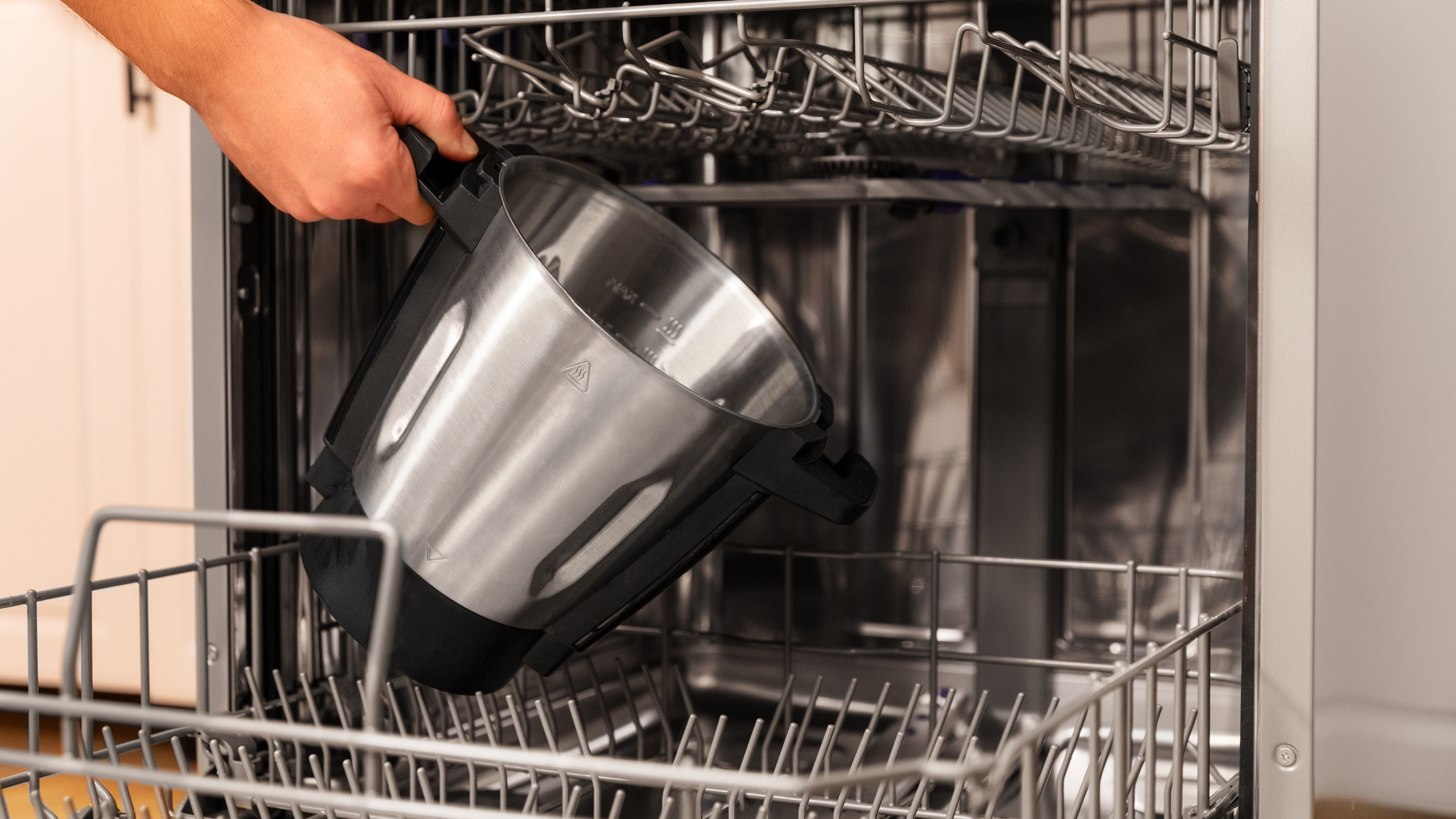 Mano colocando un cuenco de metal en un lavavajillas. Fondo de cocina.
