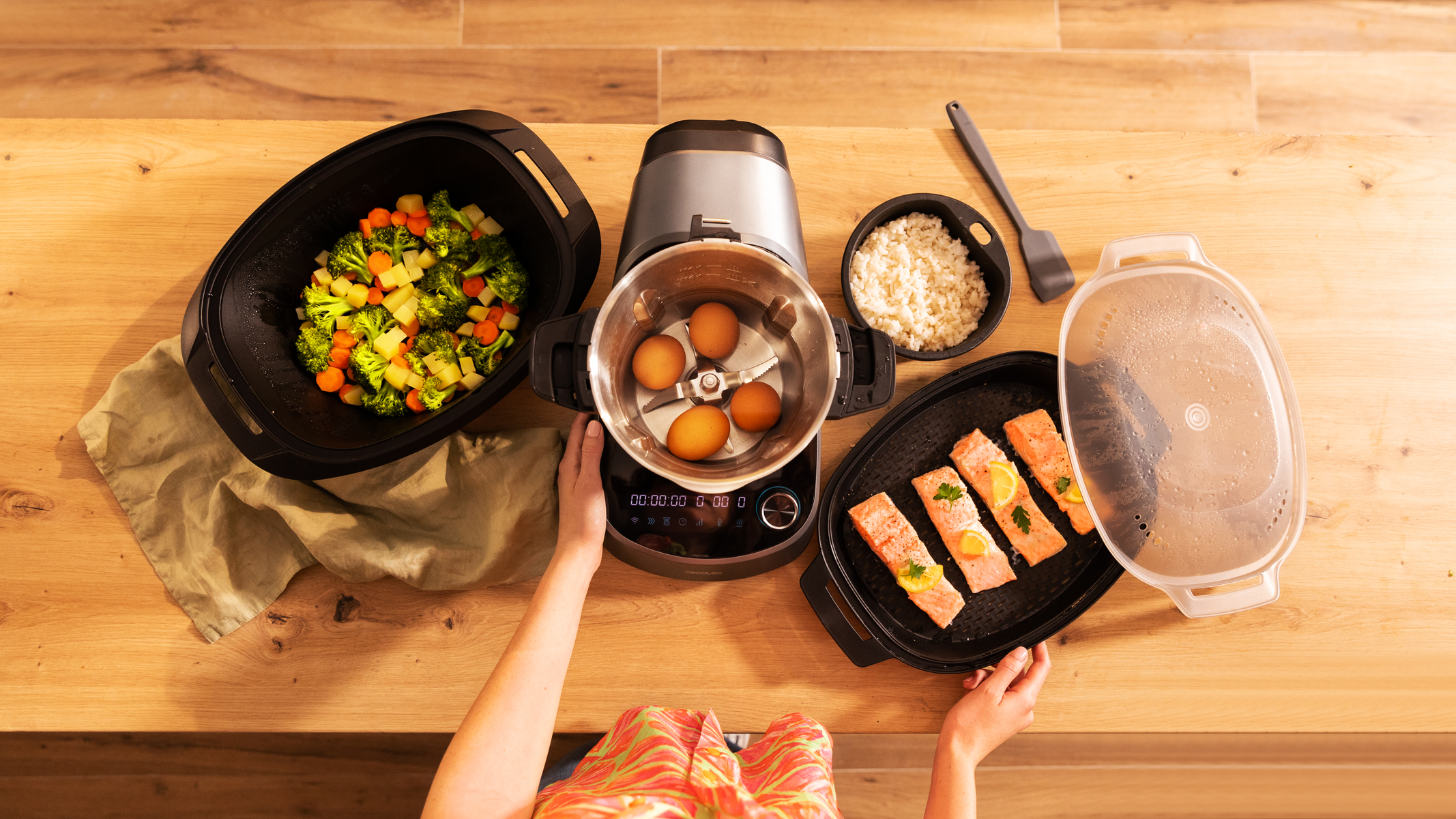 Un procesador de alimentos con verduras, huevos, arroz y pescado. Vista superior sobre una mesa de madera.