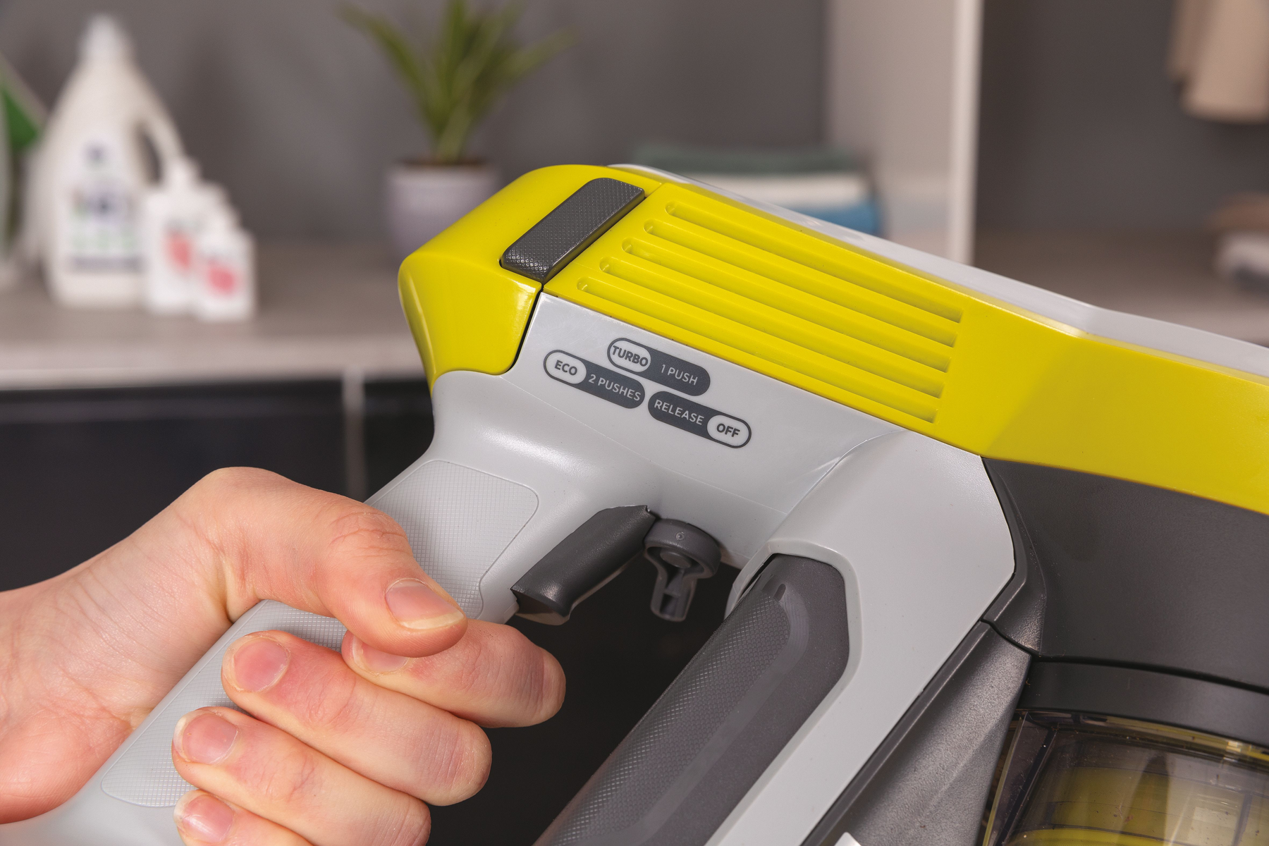Mano che usa un aspirapolvere giallo e grigio. Pulsanti Eco, Turbo e Release.