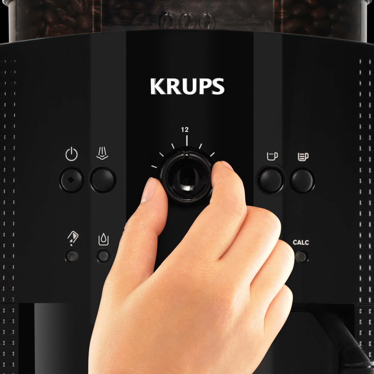 Una mano gira un dial en una cafetera negra de la marca KRUPS.