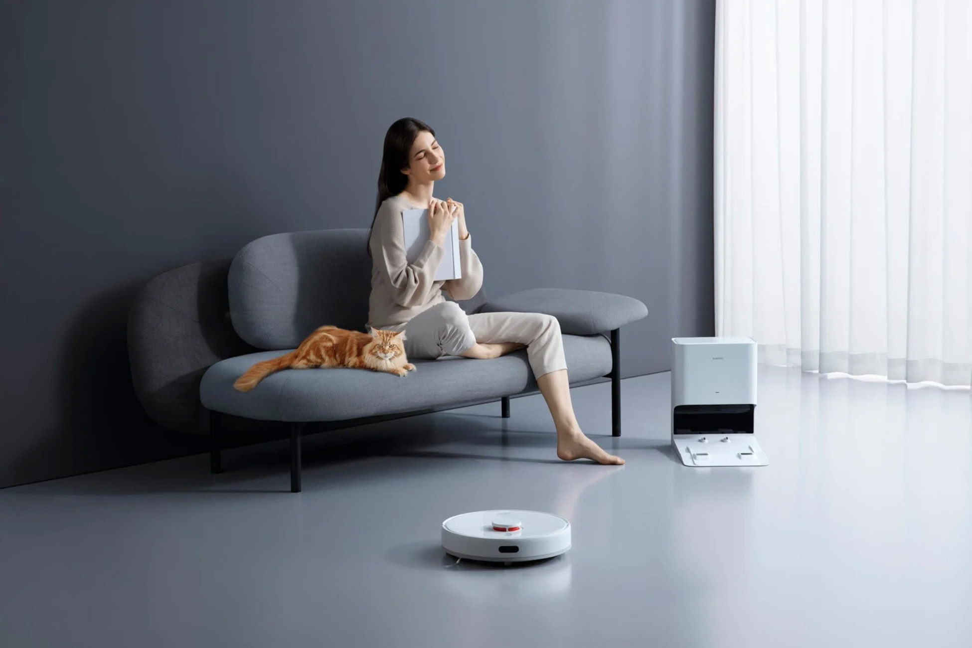 Frau auf Sofa mit Katze und Buch. Roboter-Staubsauger auf dem Boden.
