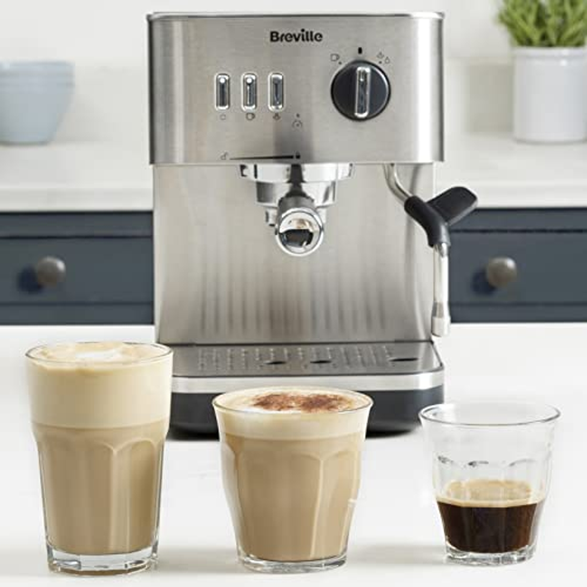 Una máquina de espresso plateada con tres bebidas y una taza. Las bebidas están en vasos.