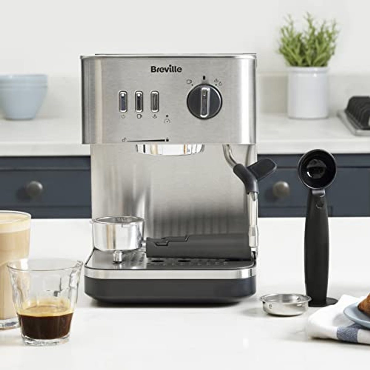 Máquina de espresso de acero inoxidable en mostrador blanco con accesorios.