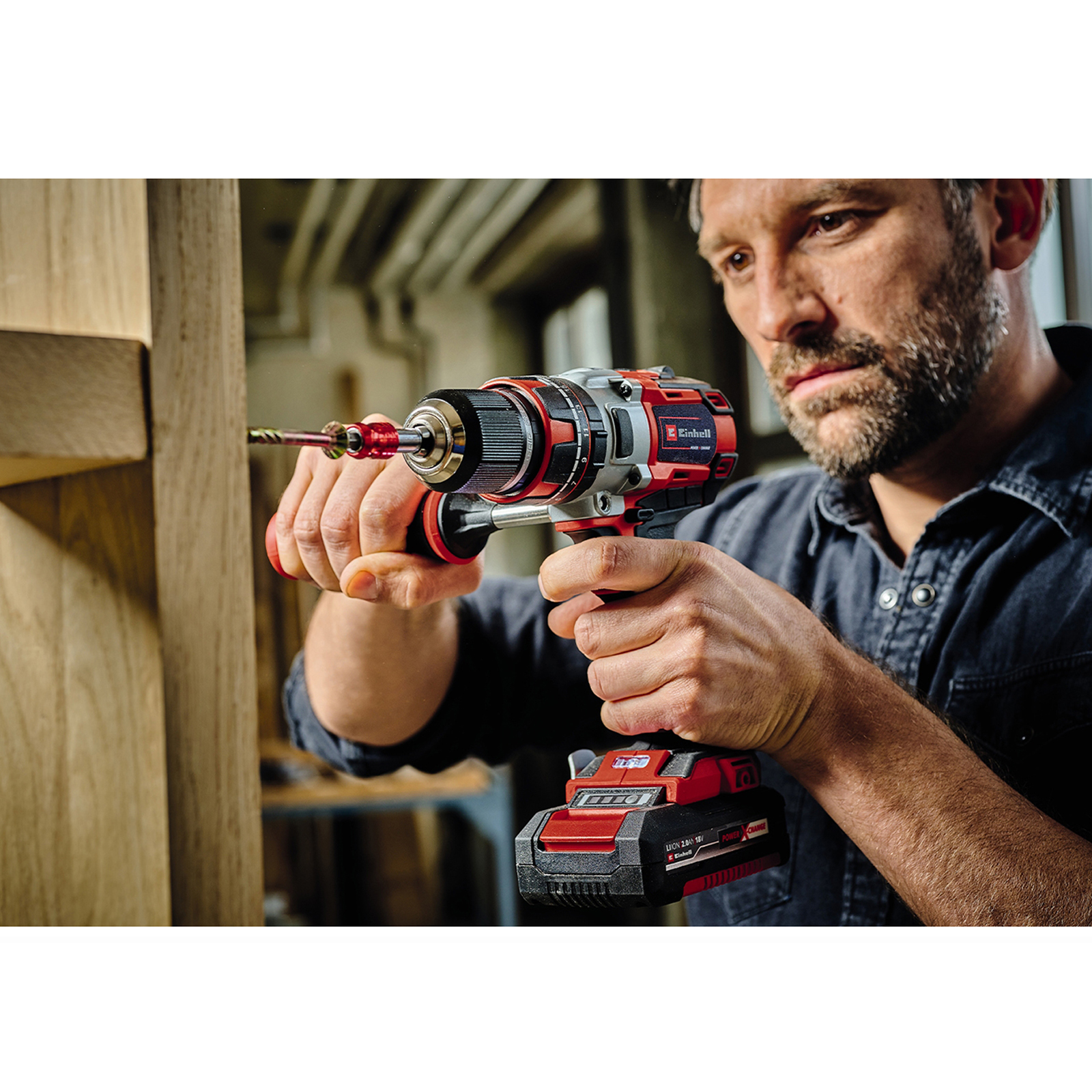Mężczyzna używa wiertarki akumulatorowej na drewnie. Czerwona i czarna wiertarka z baterią.
