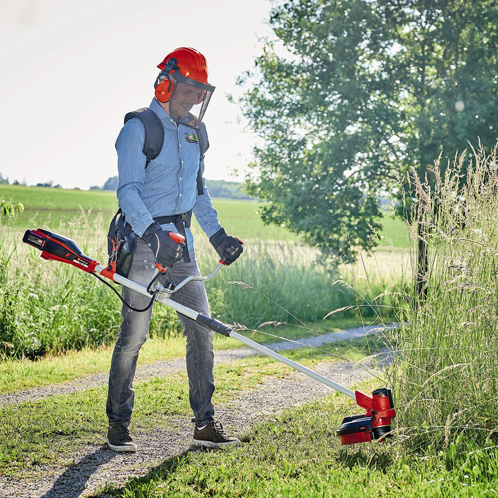 Mann benutzt Rasentrimmer auf sonnigem Feld, trägt Schutzkleidung.