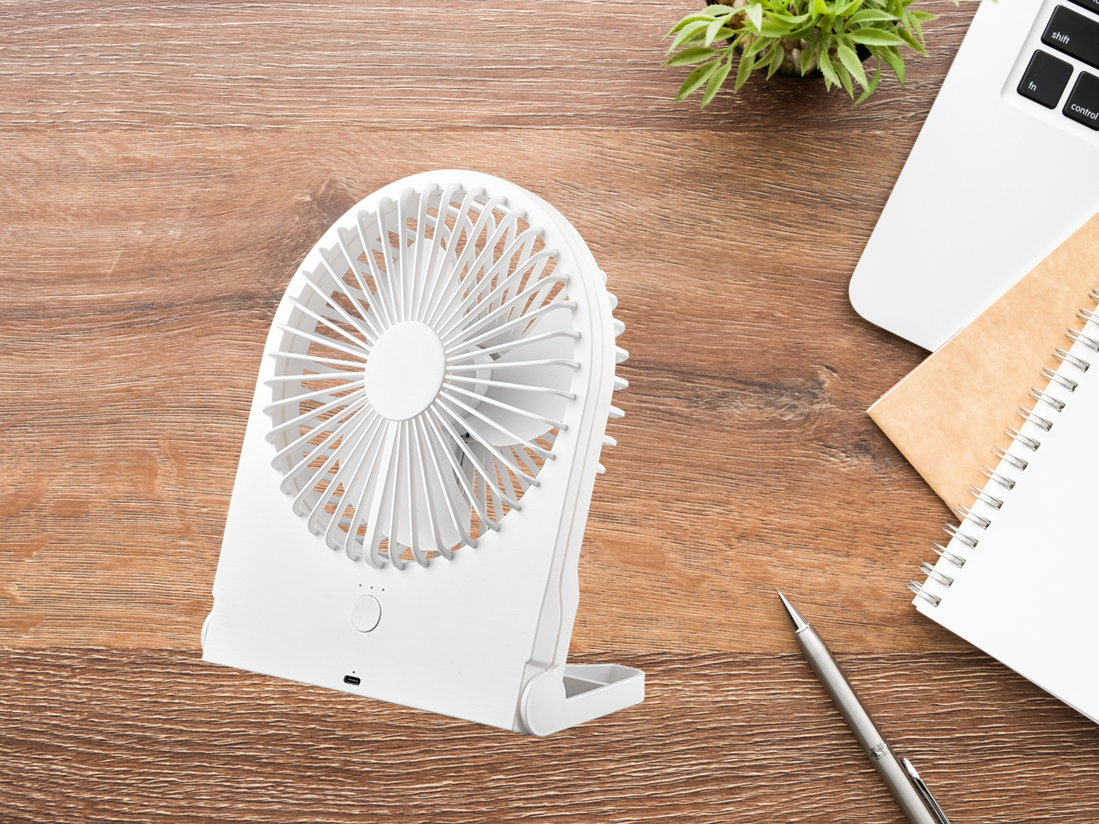 Weißer tragbarer Ventilator auf einem Holztisch mit Notizbuch, Stift und Laptop.