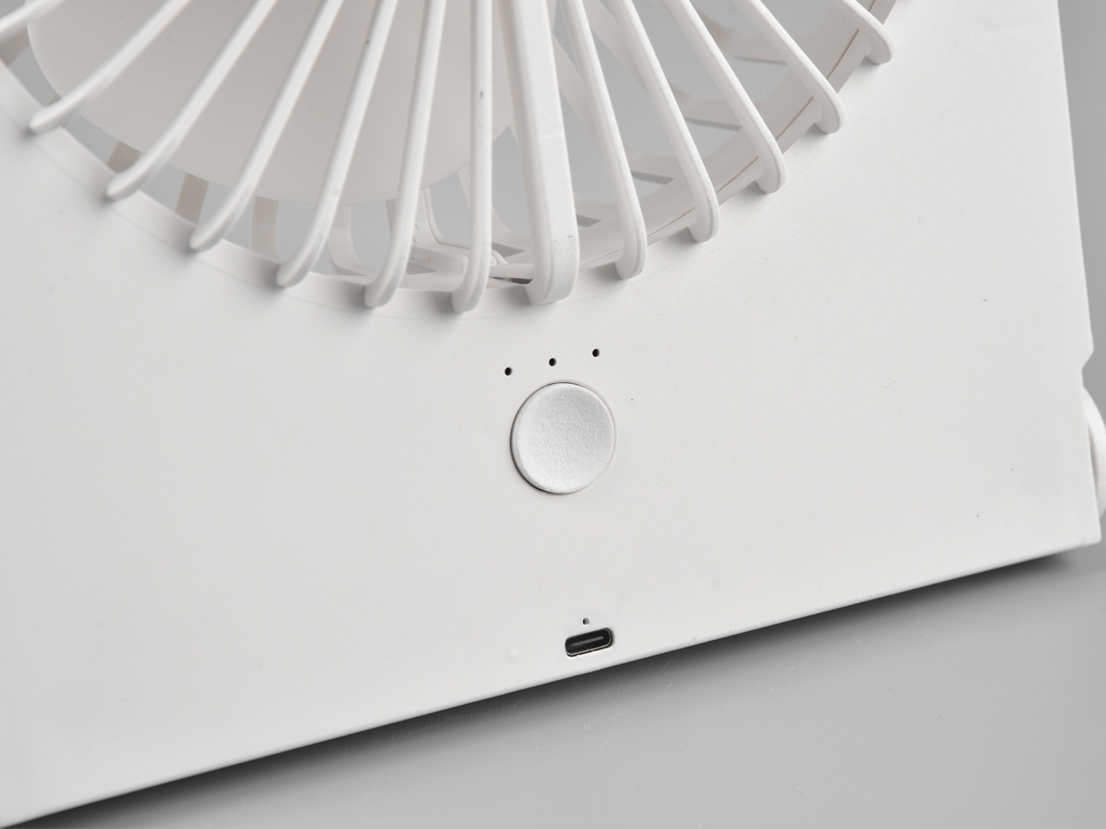 Ein weißer tragbarer Ventilator mit einem Bedienknopf und einem Ladeanschluss. Der Hintergrund ist grau.