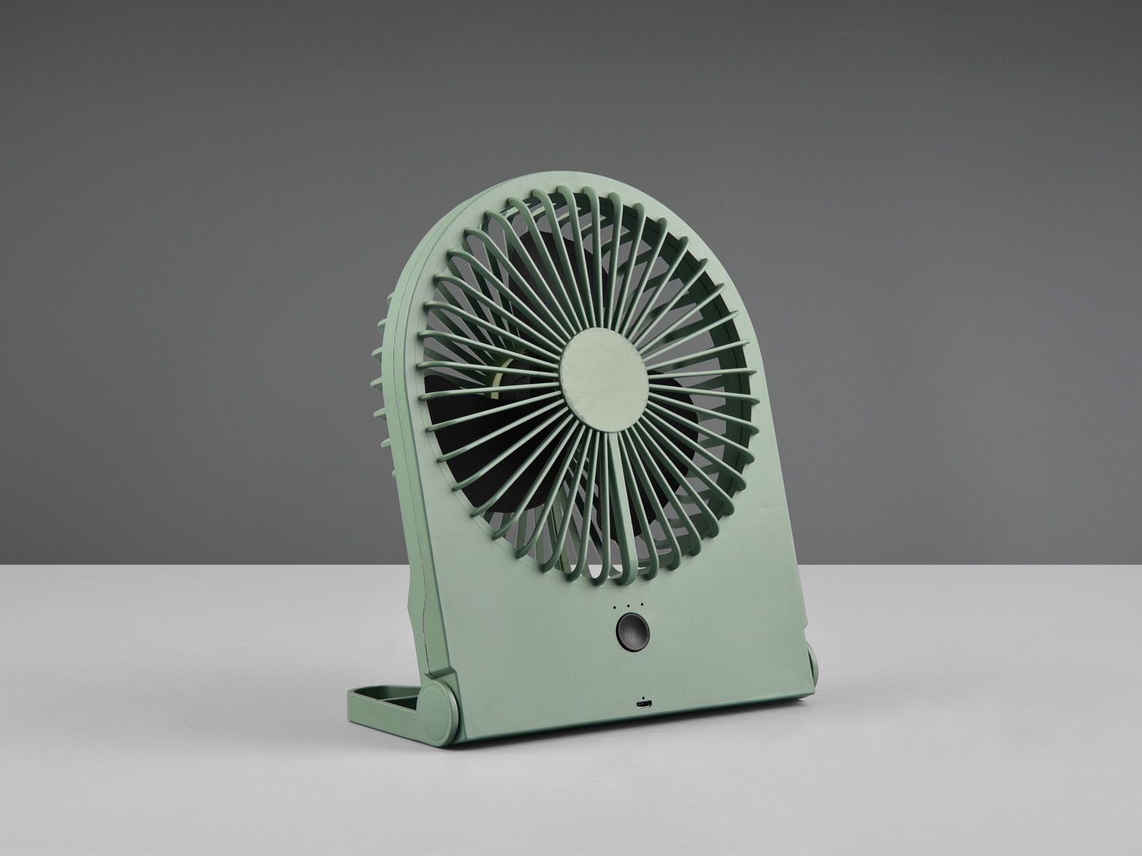 Ein grüner tragbarer Ventilator auf einer weißen Oberfläche vor grauem Hintergrund. Er ist abgewinkelt.