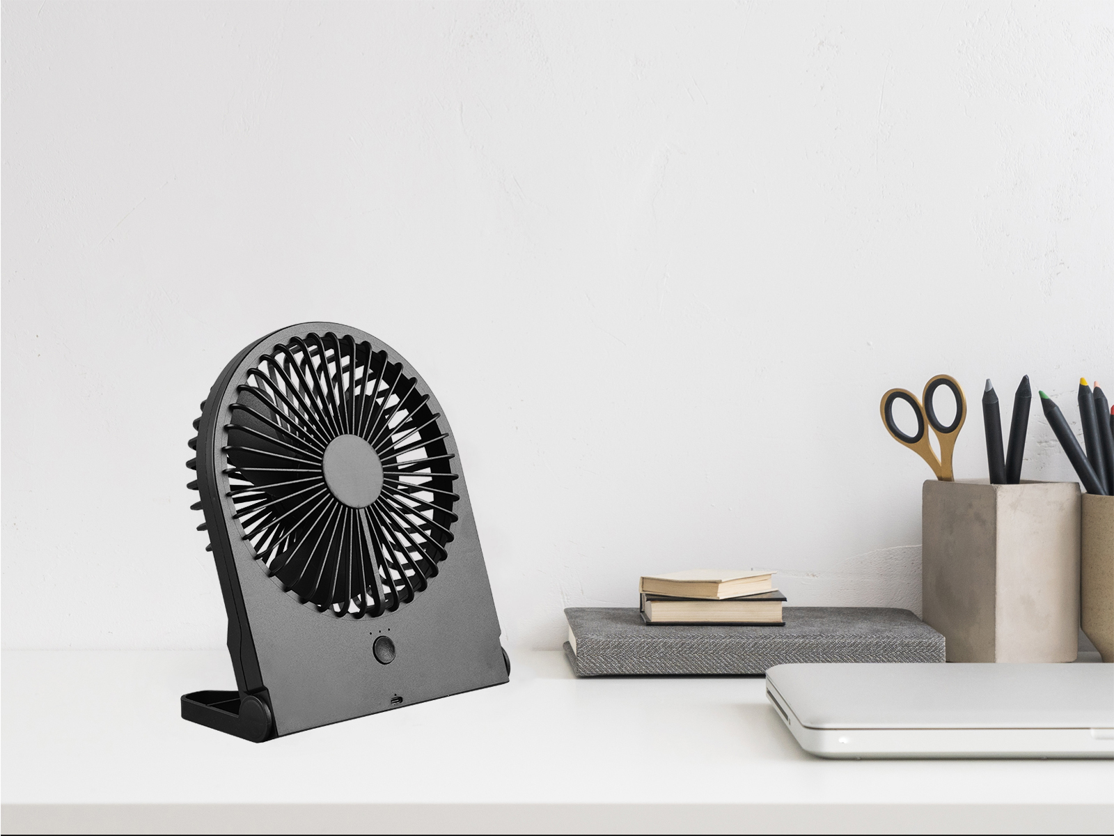 Schwarzer Ventilator auf weißem Schreibtisch mit Büromaterial.