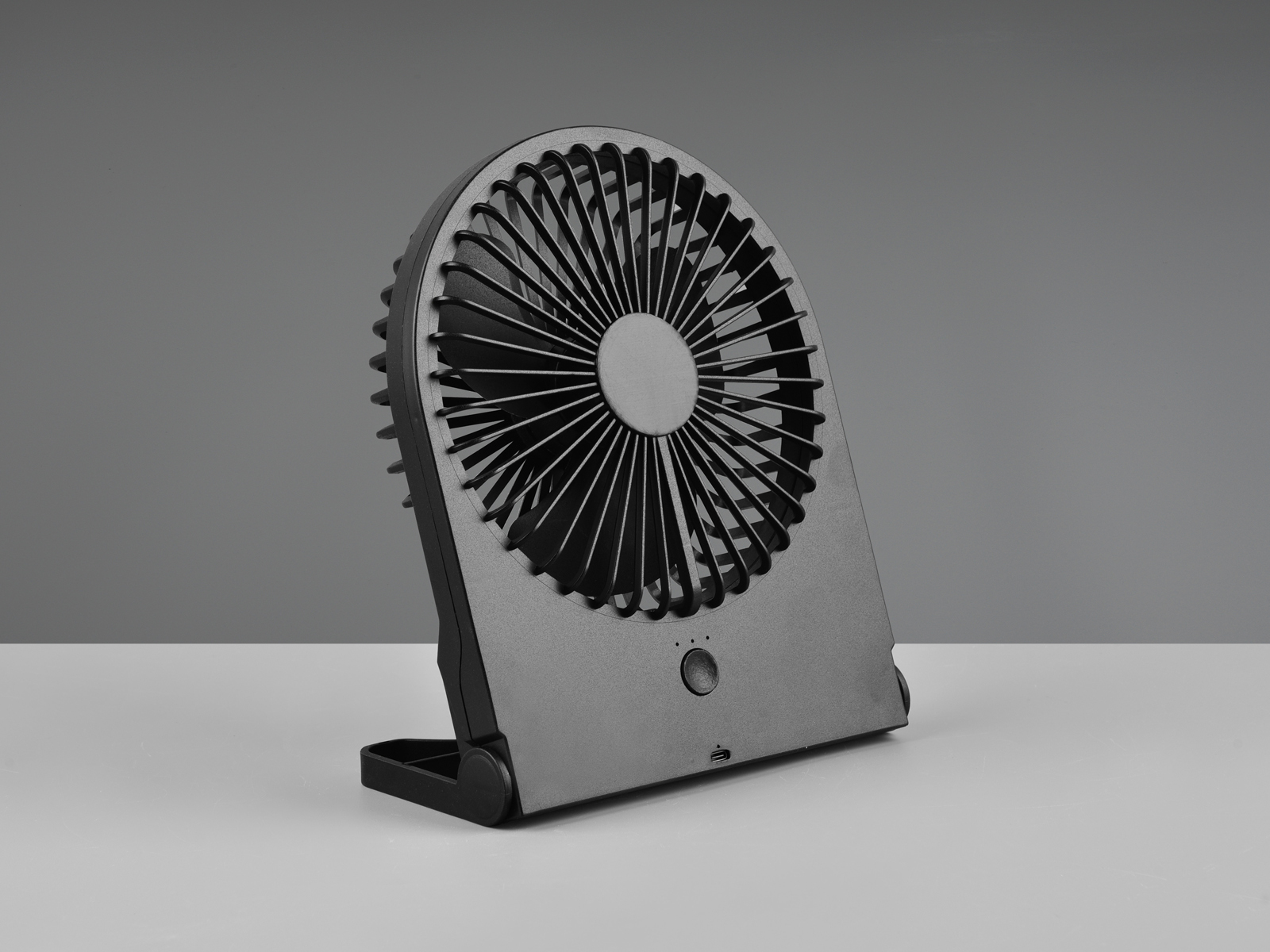Schwarzer tragbarer Ventilator mit geschwungenem Design. Der Ventilator steht auf weißem Untergrund vor grauem Hintergrund.