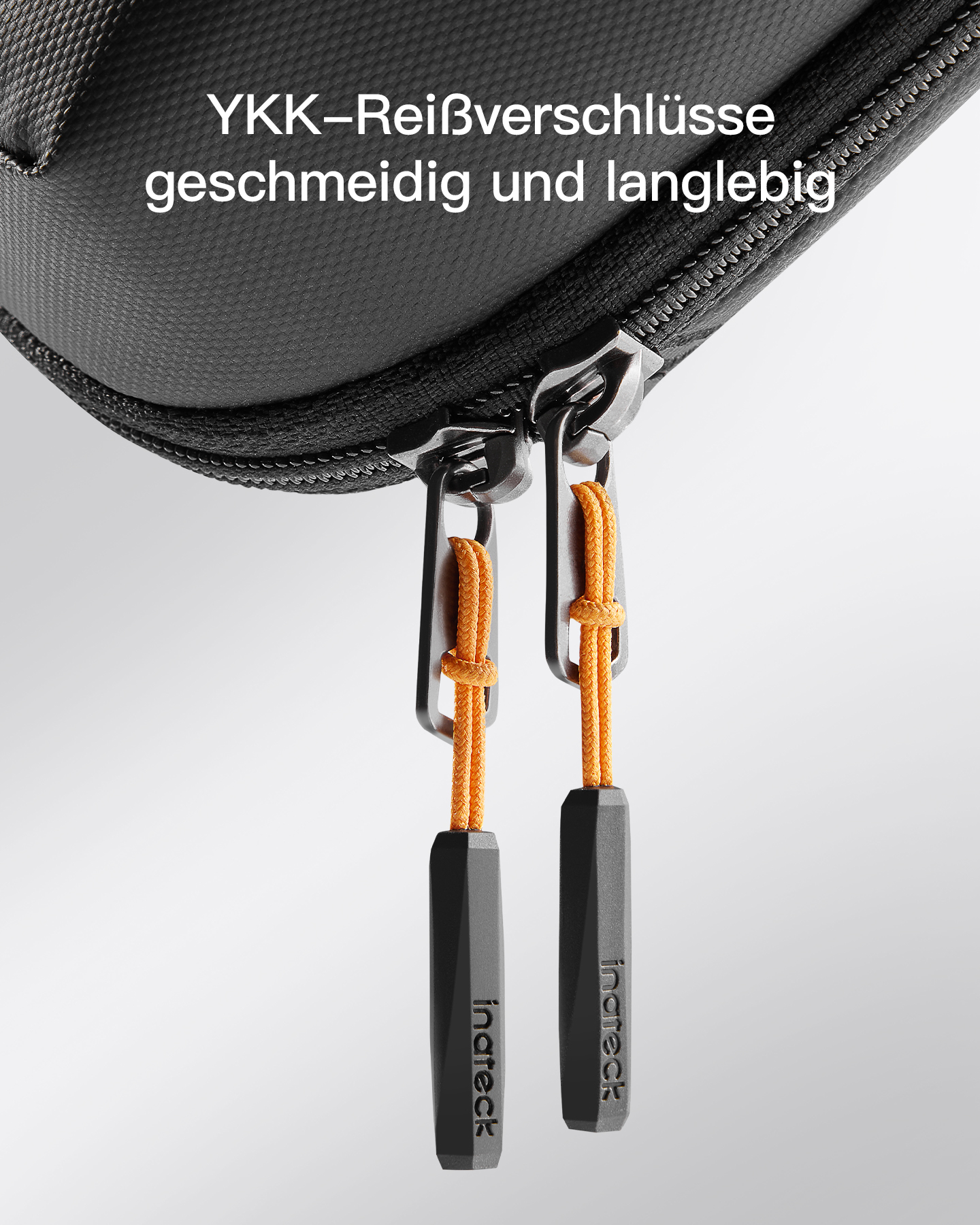 Schwarze Tasche mit YKK-Reißverschlüssen und orangefarbenen Zügen. Text oben auf Deutsch.