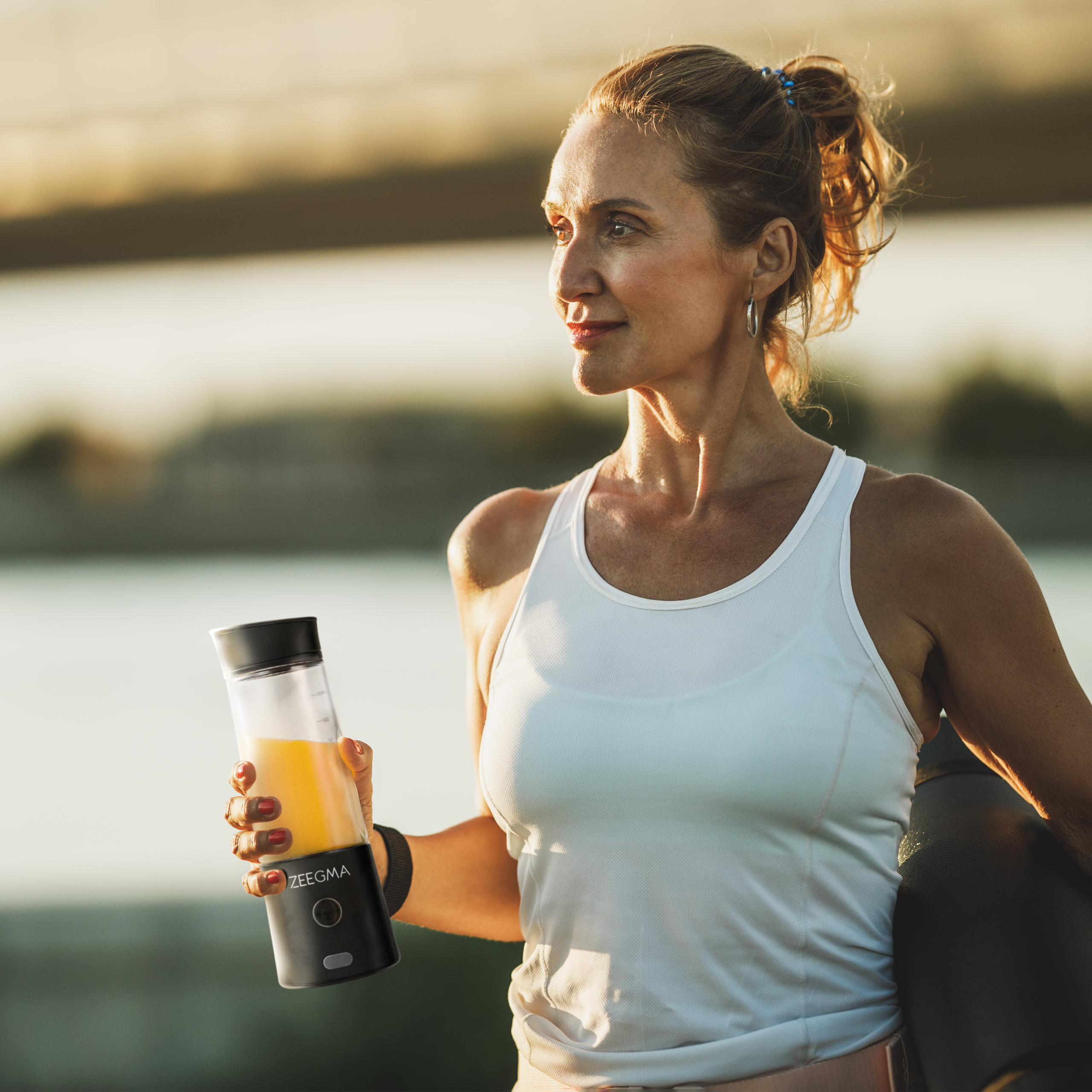 Kobieta trzymająca czarny i przezroczysty blender do soku na zewnątrz, odwracając wzrok.
