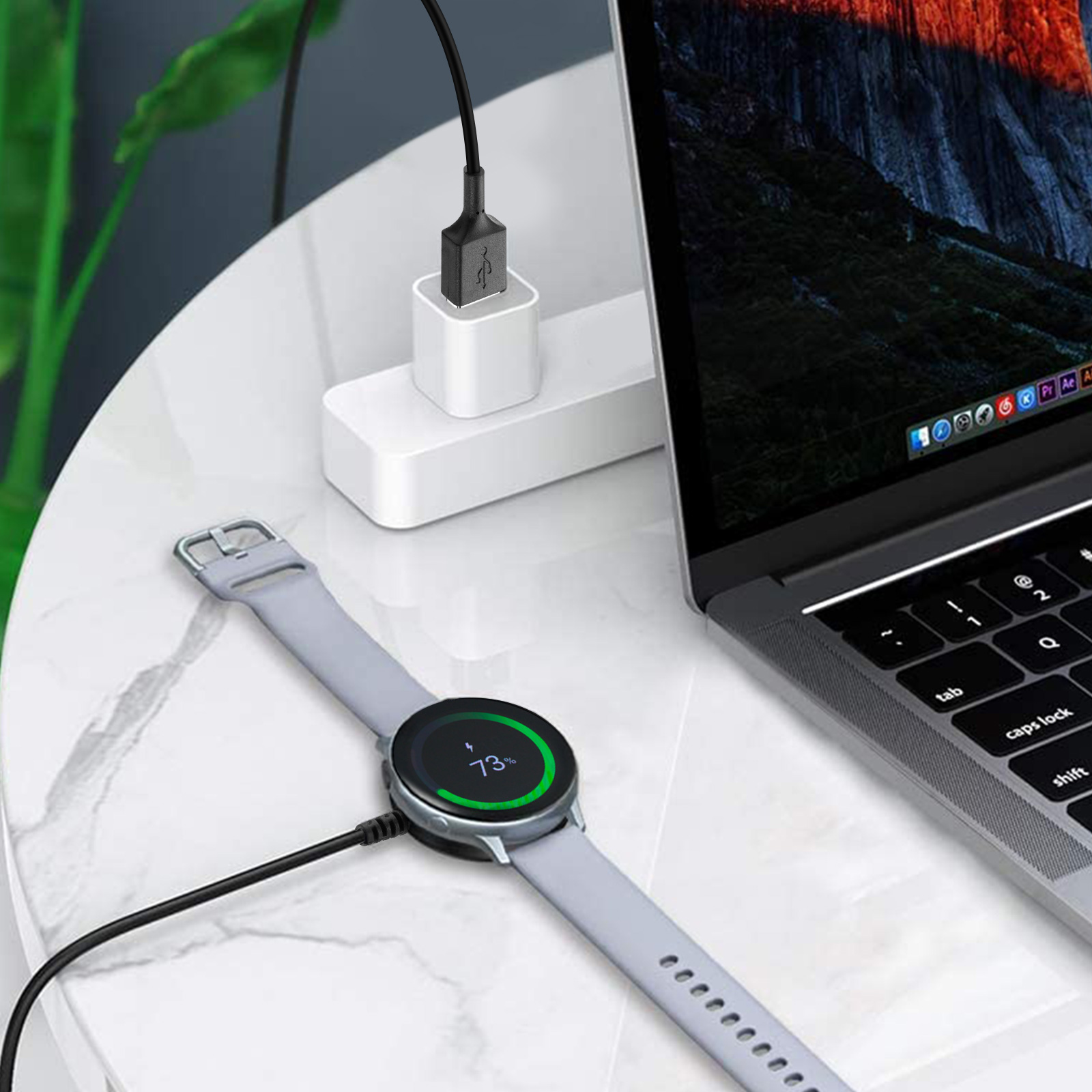 Un smartwatch se está cargando junto a una laptop. Un cargador USB está conectado a una regleta.
