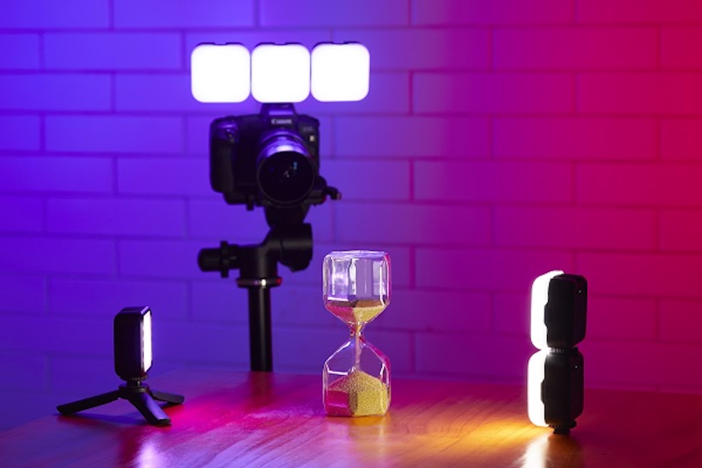 Aparat na statywie, klepsydra i dwa światła na stole.