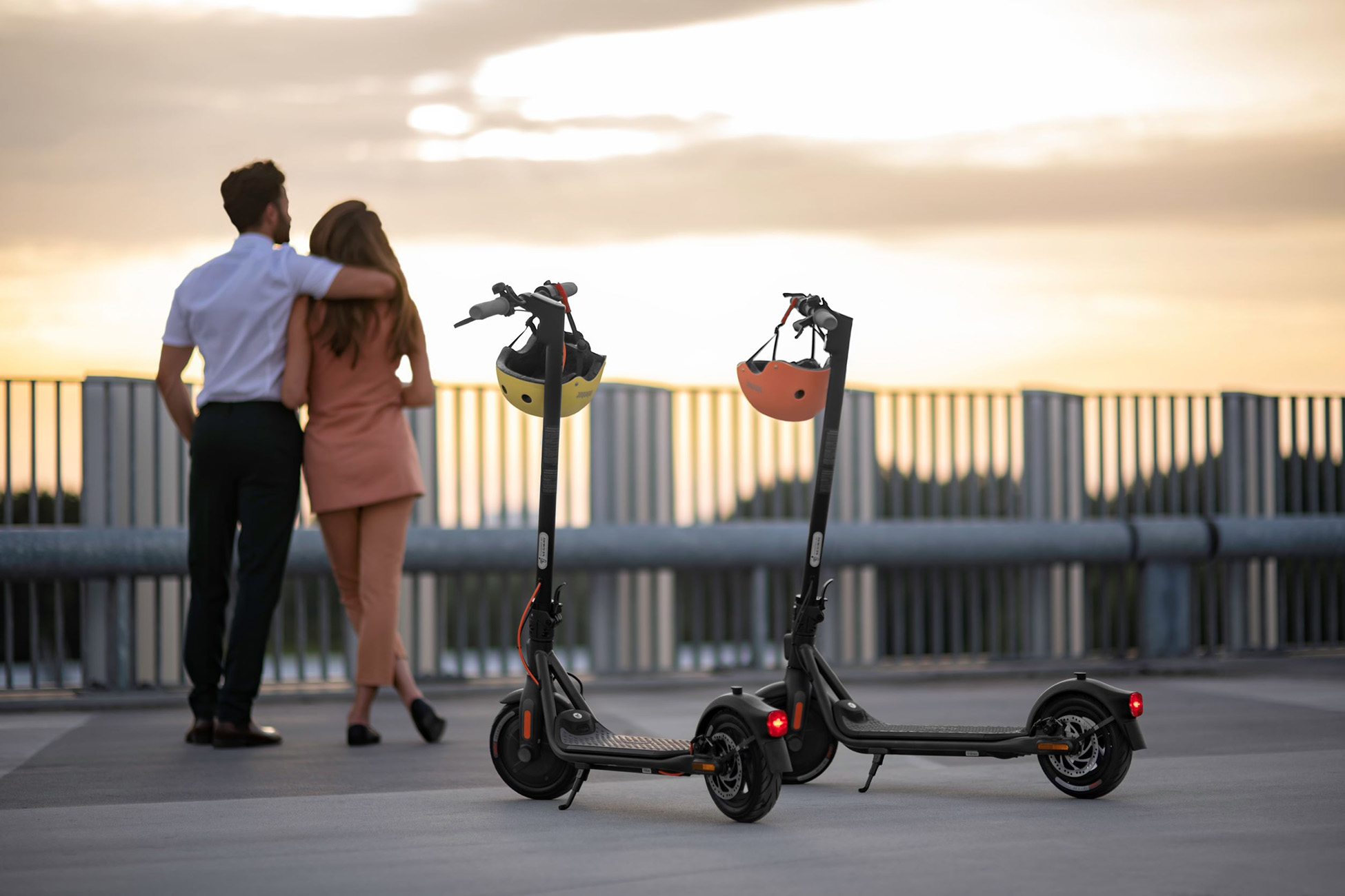 Zwei Roller mit Helmen vor einem Paar, vor einem Sonnenuntergang.