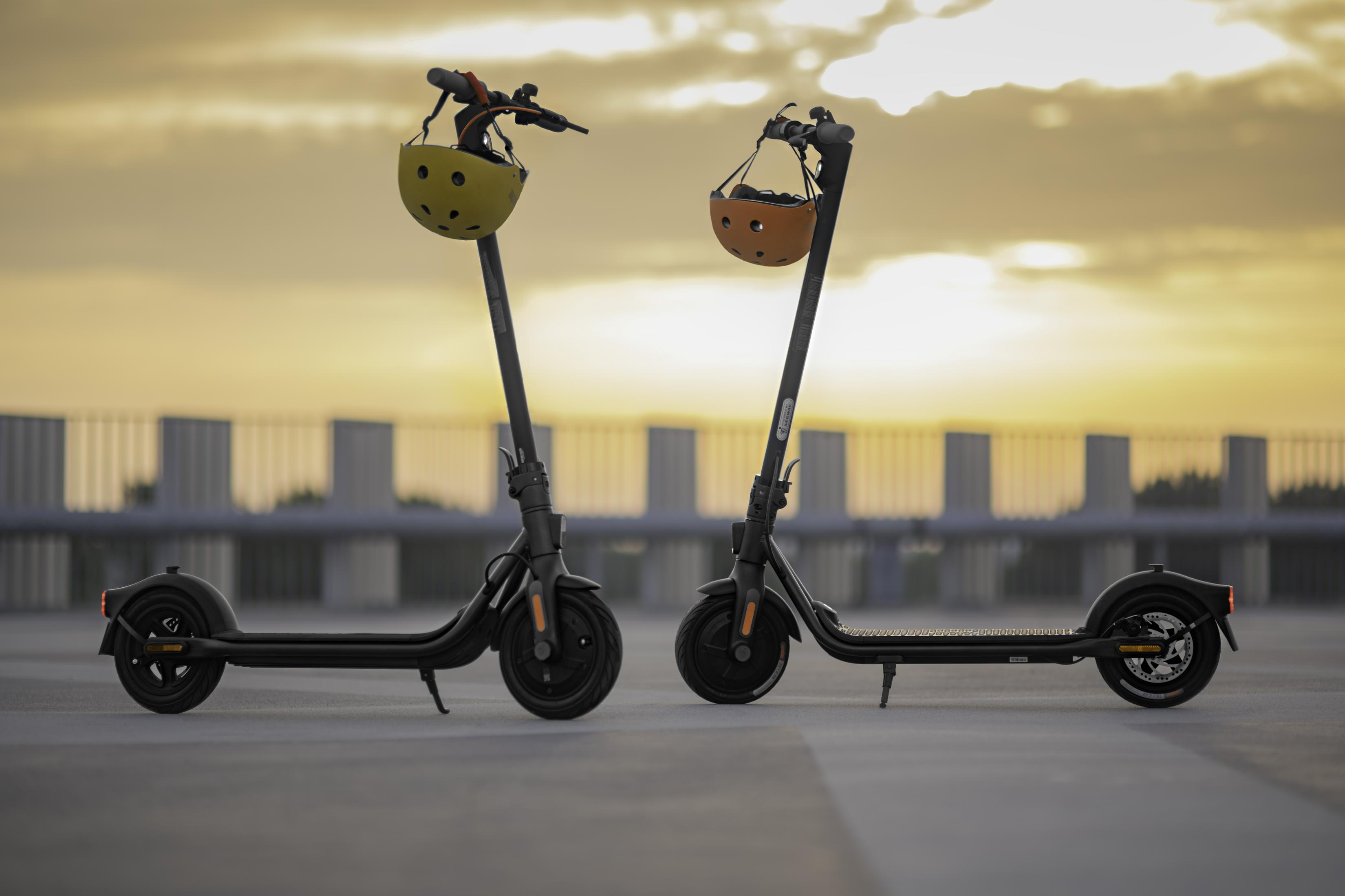 Zwei schwarze Roller mit Helmen am Lenker, geparkt auf Beton, Sonnenuntergang im Hintergrund.