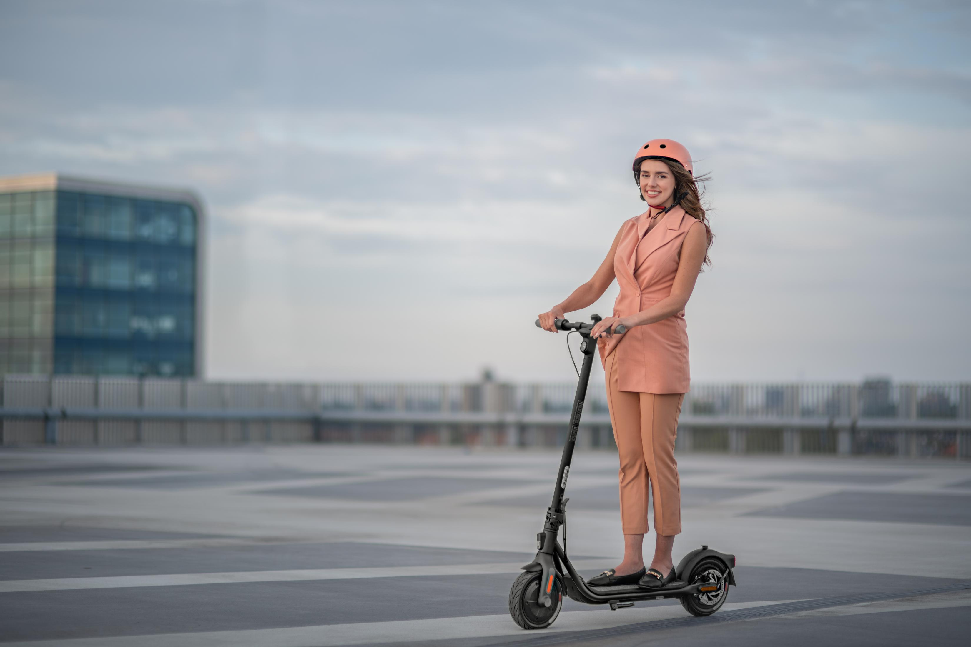 Eine Frau im rosa Anzug fährt auf einem Dach mit einem Roller.