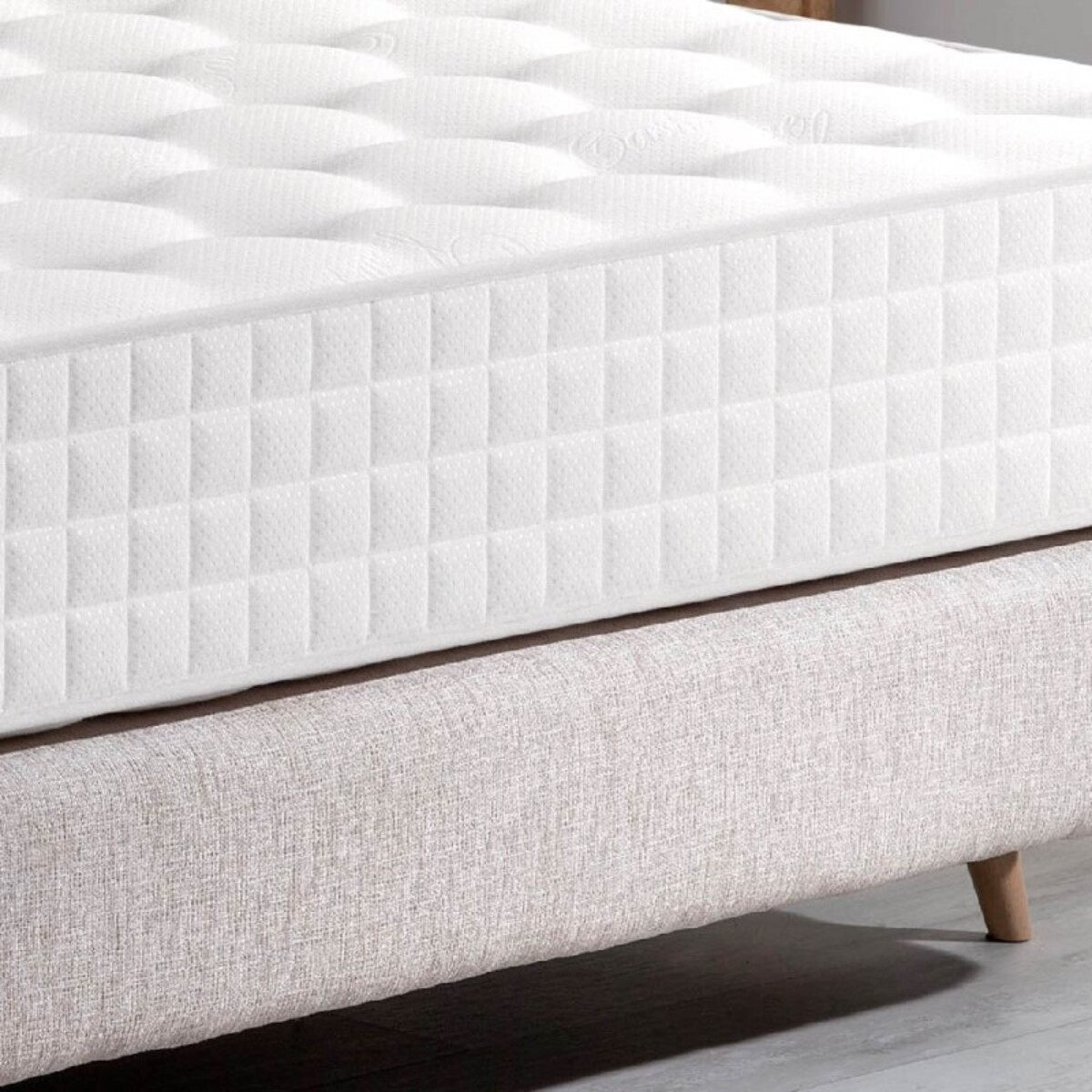 Primer plano de un colchón blanco sobre un marco de cama. Patrón acolchado.