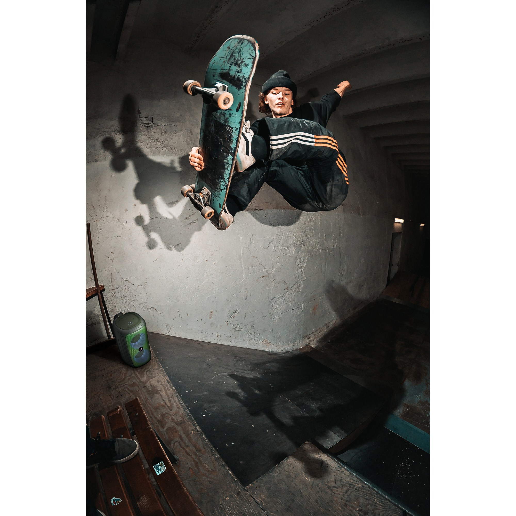 Skejt w powietrzu, z turkusową deskorolką, wewnątrz betonowej konstrukcji.