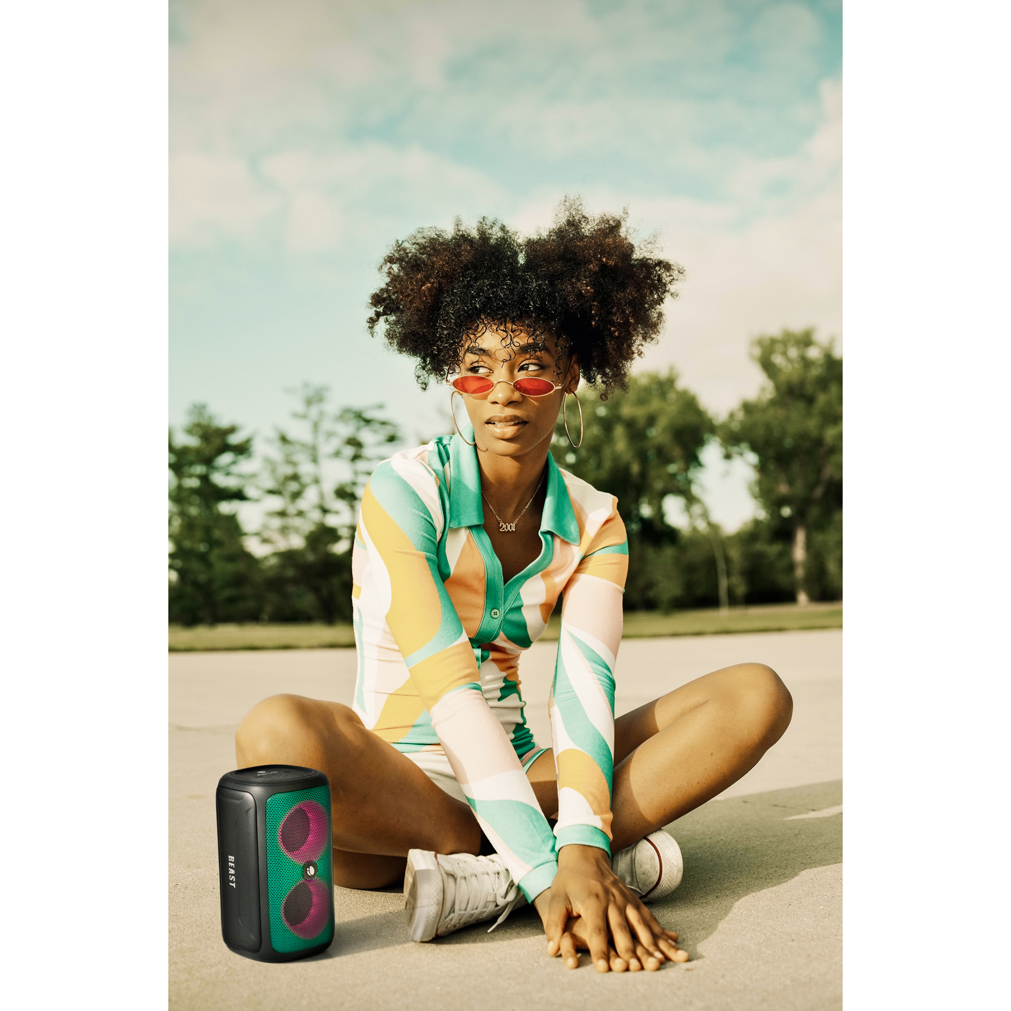 Une jeune femme est assise avec un haut-parleur. Elle porte des lunettes de soleil et une chemise colorée.