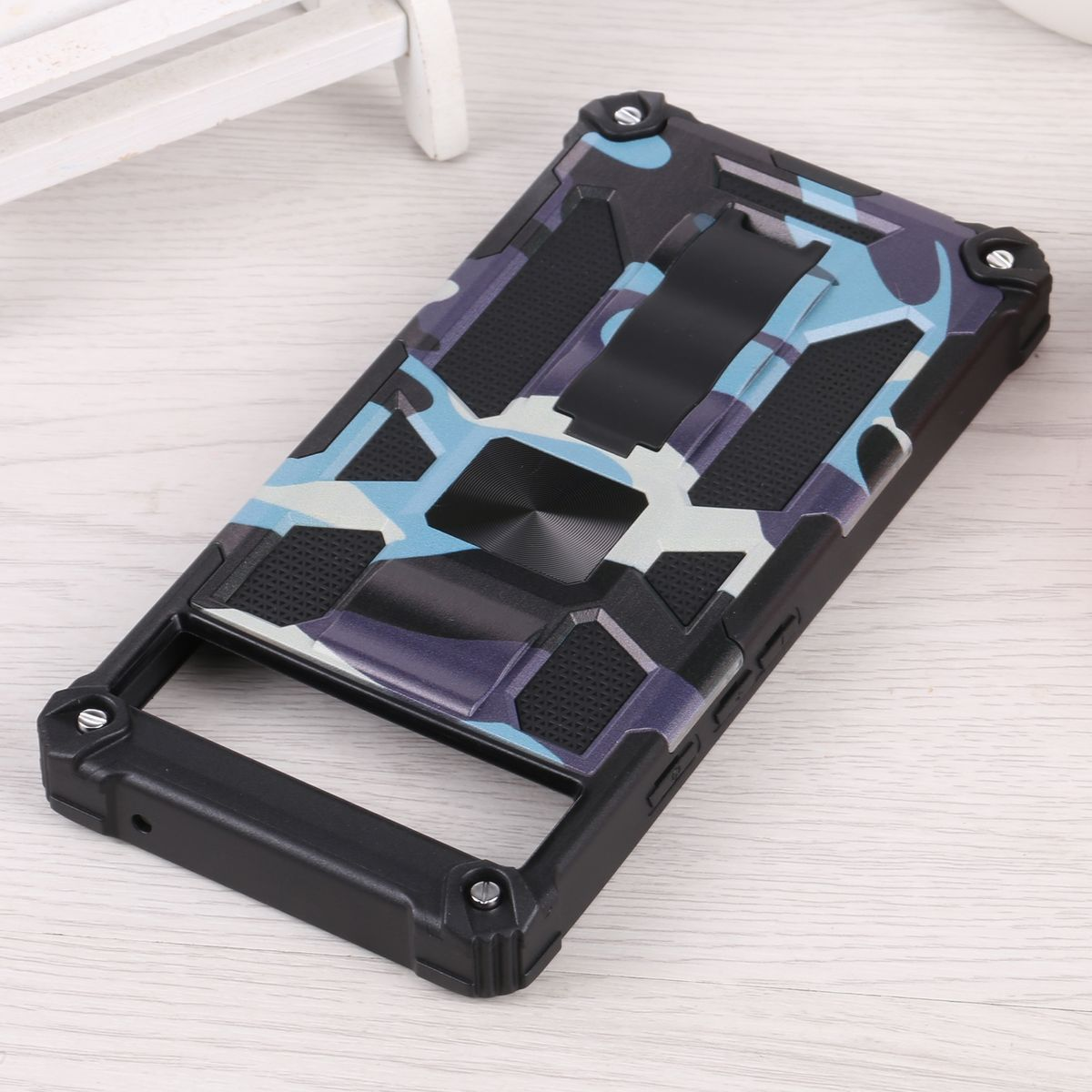 Camouflage-Handyhülle mit Ständer auf Holzoberfläche. Schwarze Kanten und blaues, graues und weißes Muster.