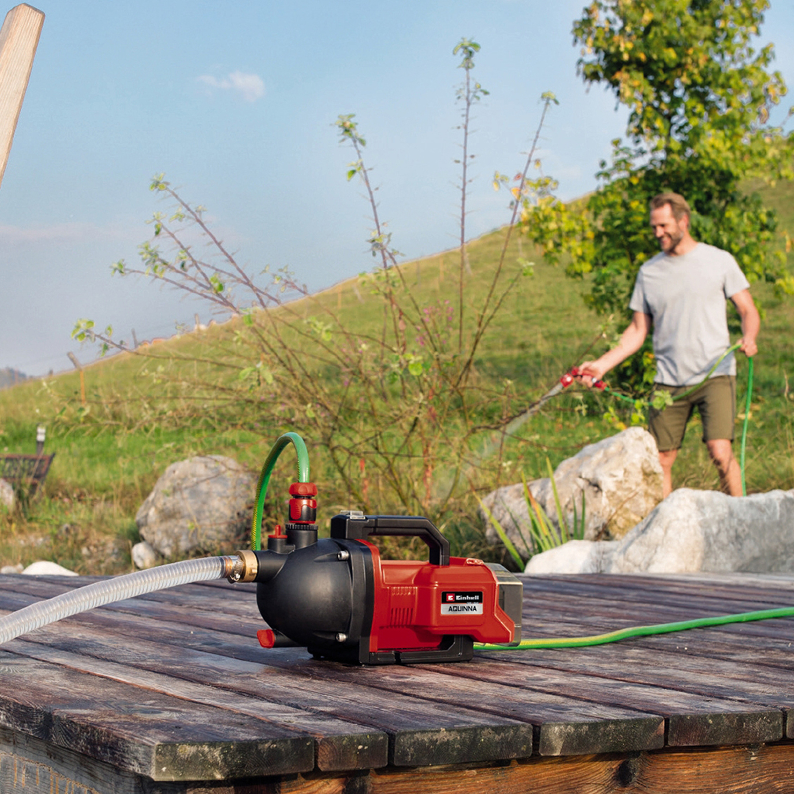 Mężczyzna podlewający rośliny wężem w pobliżu pompy wodnej. Pompa jest czerwono-czarna.