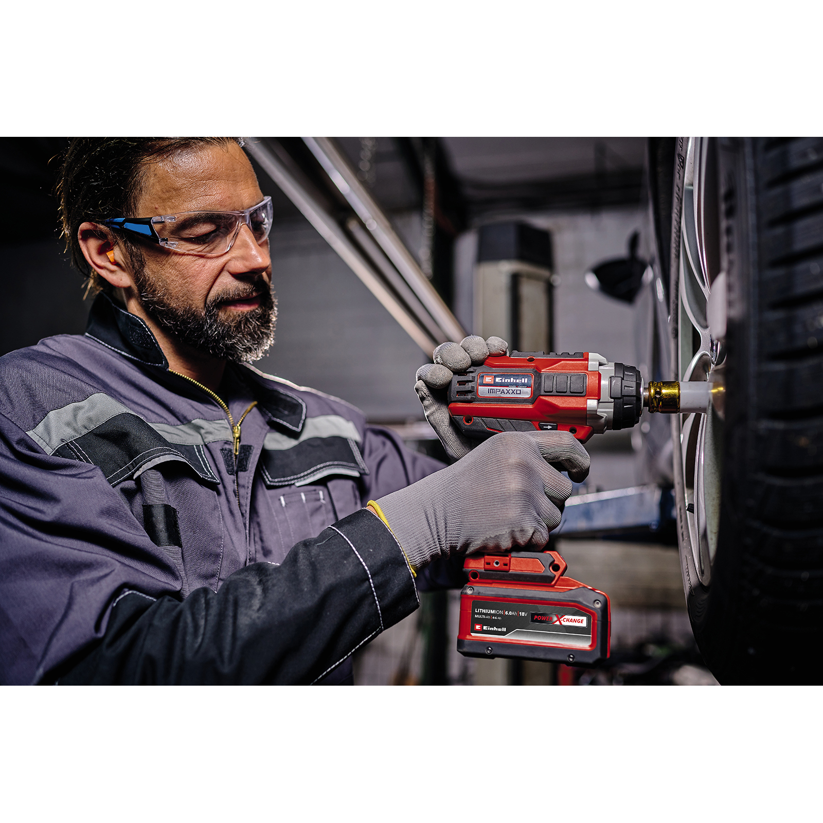 Mężczyzna w okularach ochronnych używa czerwono-czarnego klucza udarowego do demontażu opony.