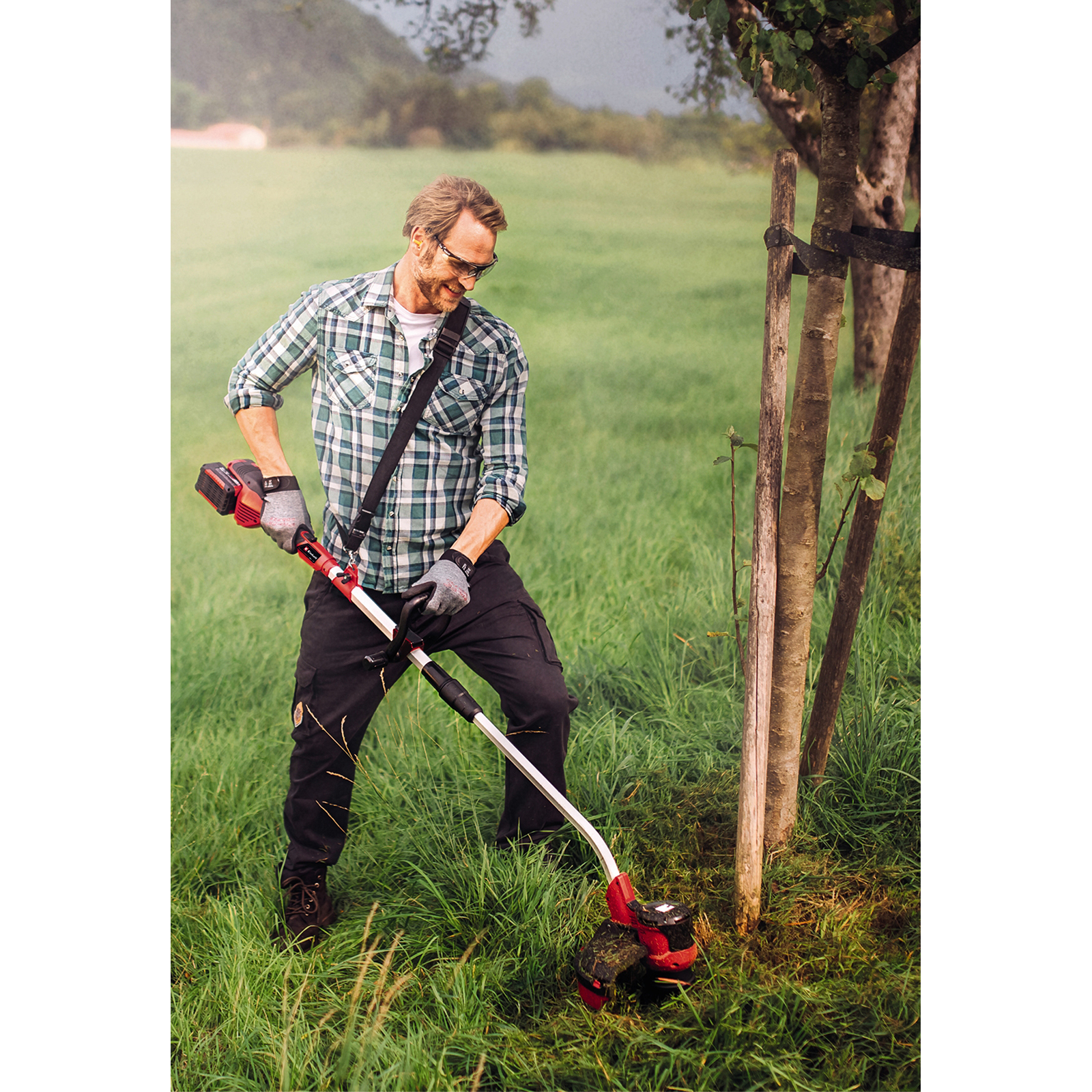 Hombre usando un cortacésped rojo y negro sobre césped cerca de árboles en un día nublado.