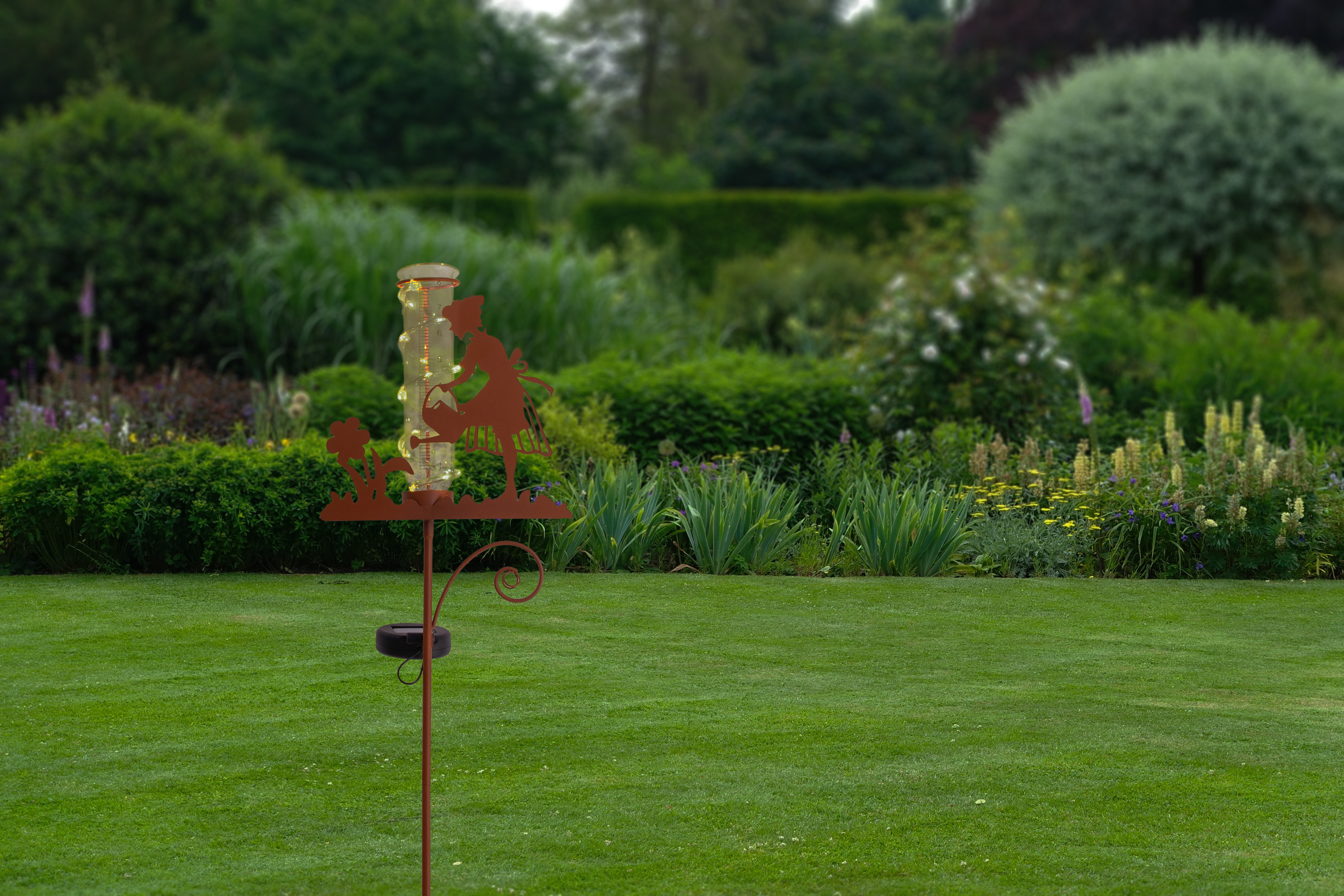 Gartenszene mit dekorativen Lichtern an einem Pfahl. Grünes Gras und Sträucher im Hintergrund.