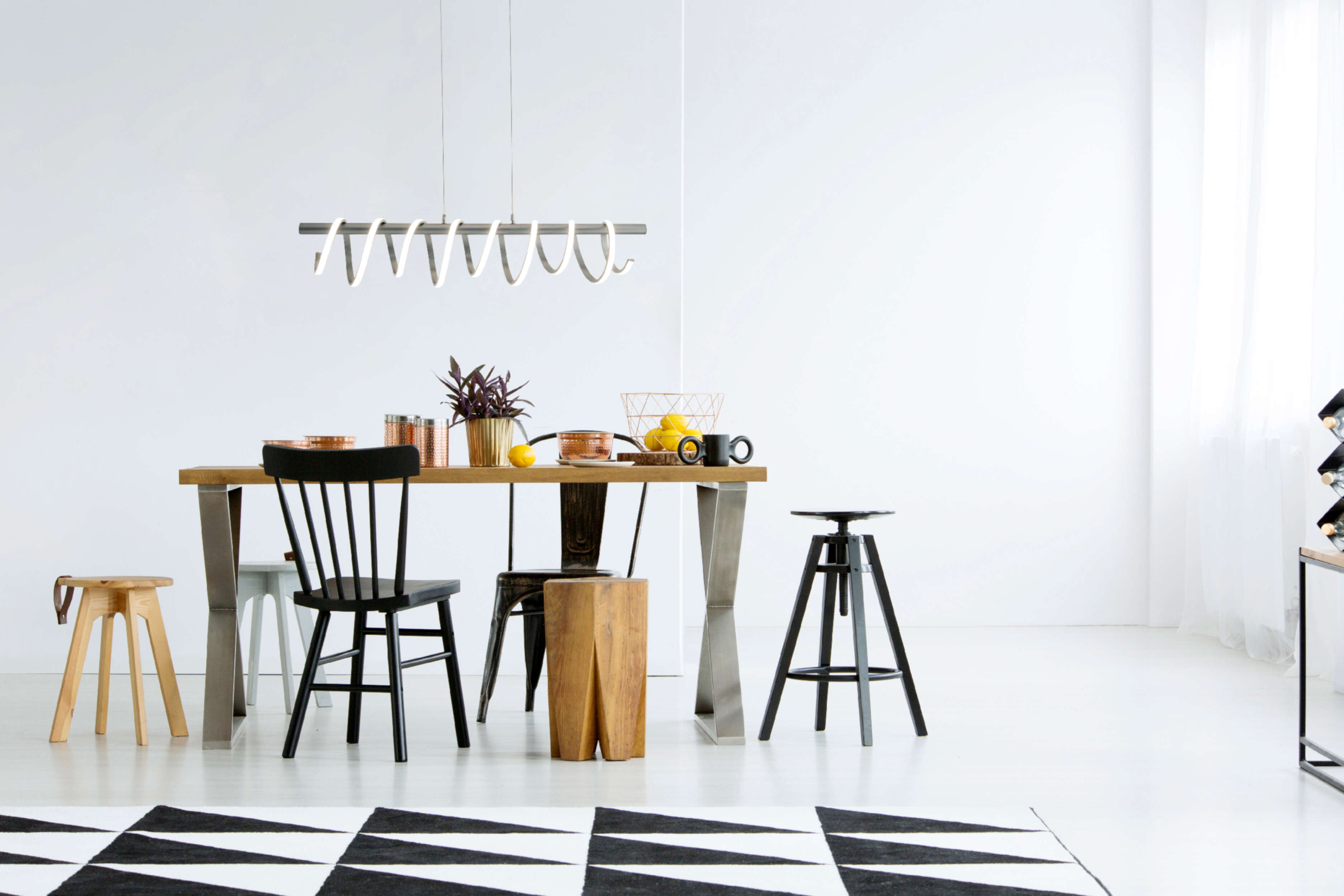 Esszimmer mit Holztisch, Stühlen und geometrischem Teppich. Weiße Wände und moderne Leuchte.