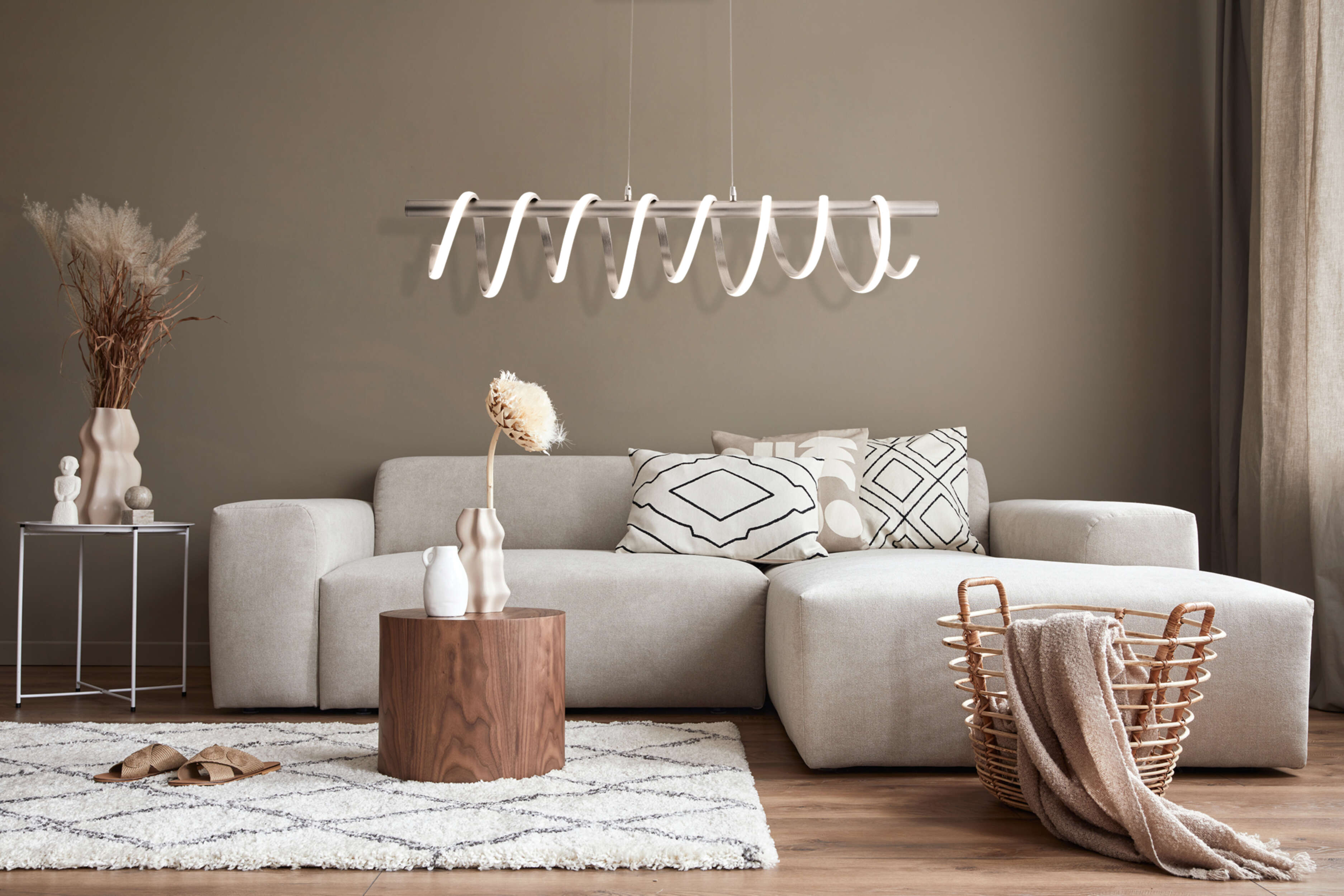Ein Wohnzimmer mit weißem Sofa, Kissen, Holztisch und moderner Lampe.
