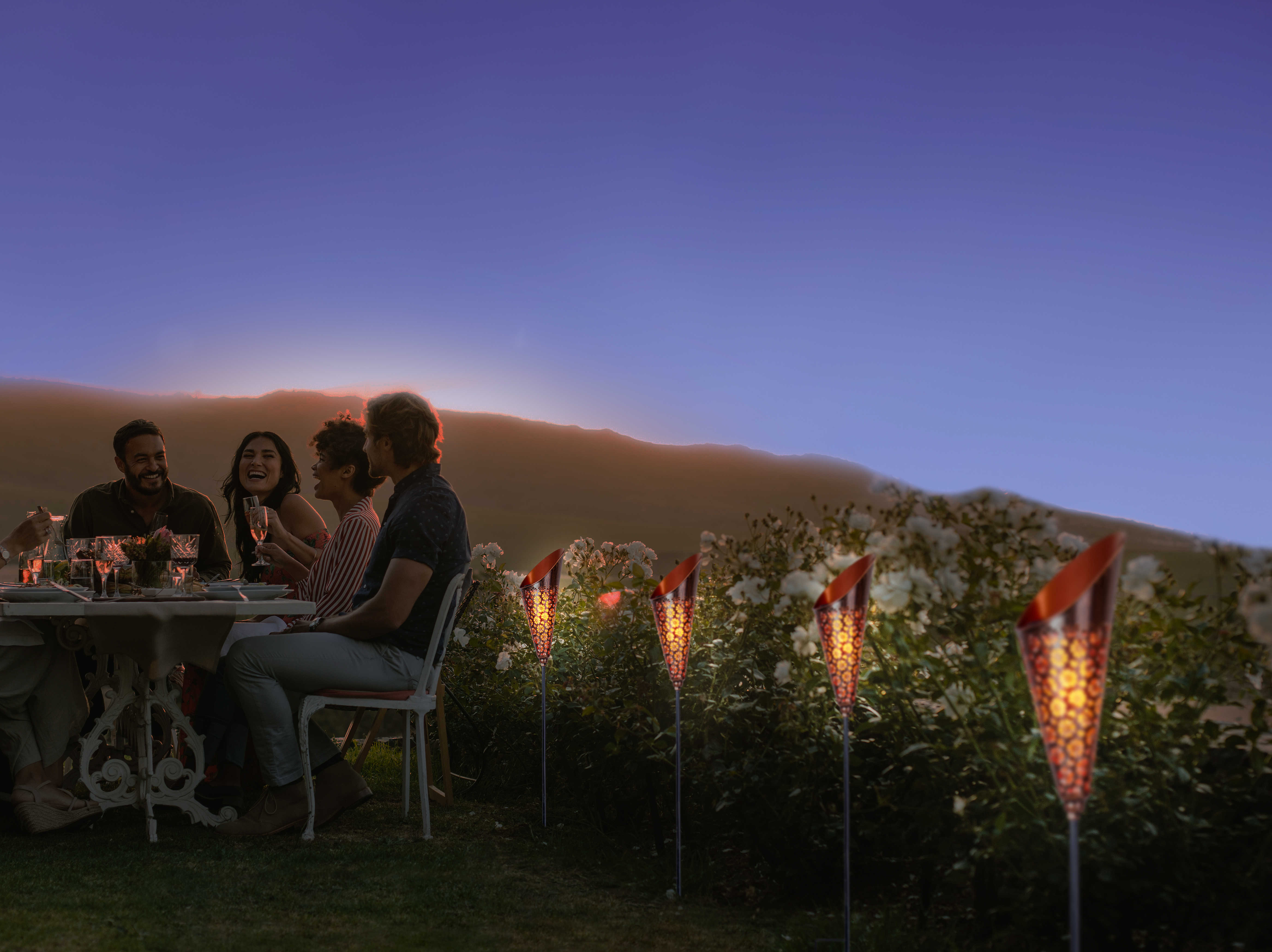 Menschen bei einem Abendessen im Freien mit Solarleuchten im Hintergrund.