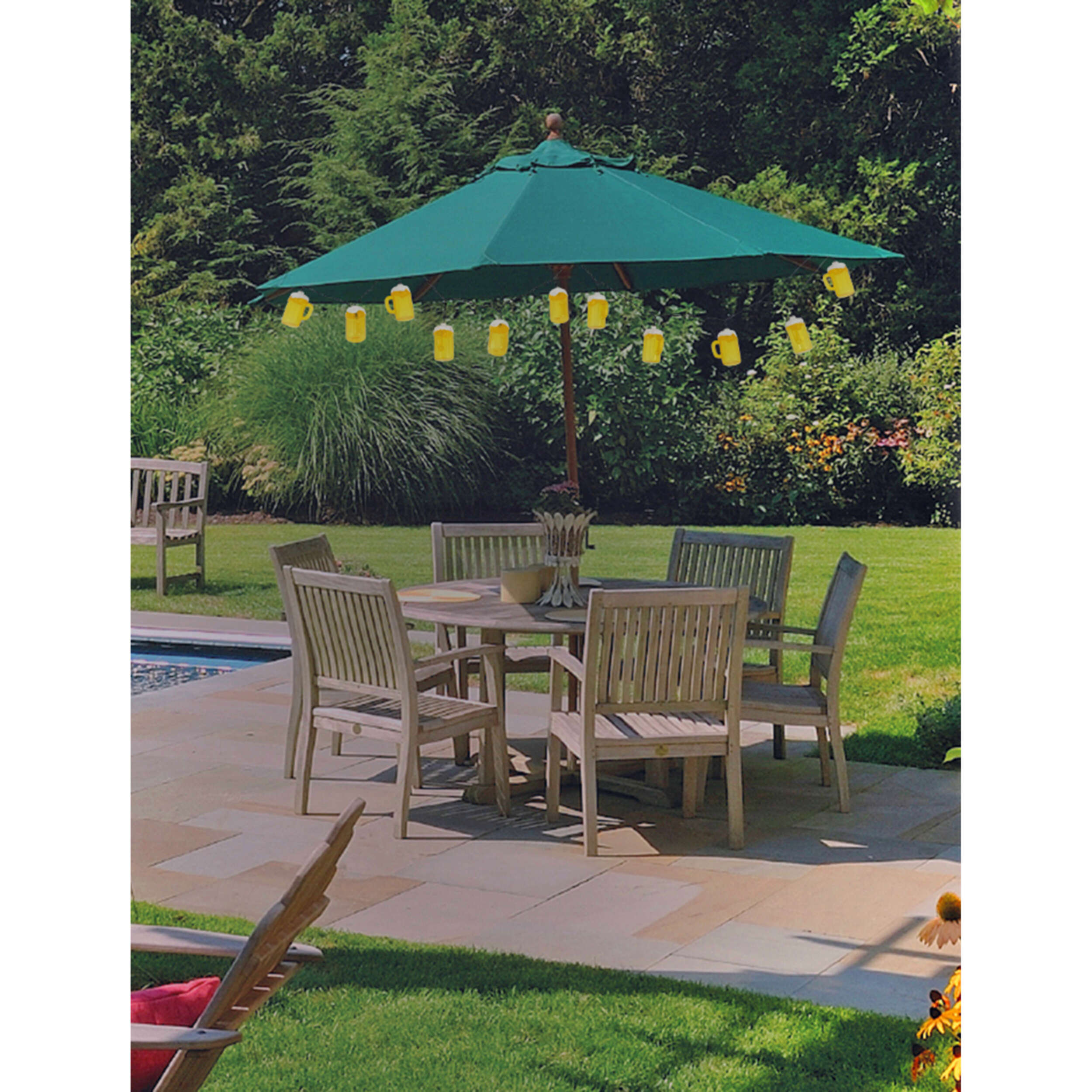 Terrassensetting mit grünem Sonnenschirm, Holztisch, Stühlen und Bierkrügen. Hintergrund mit Bäumen.